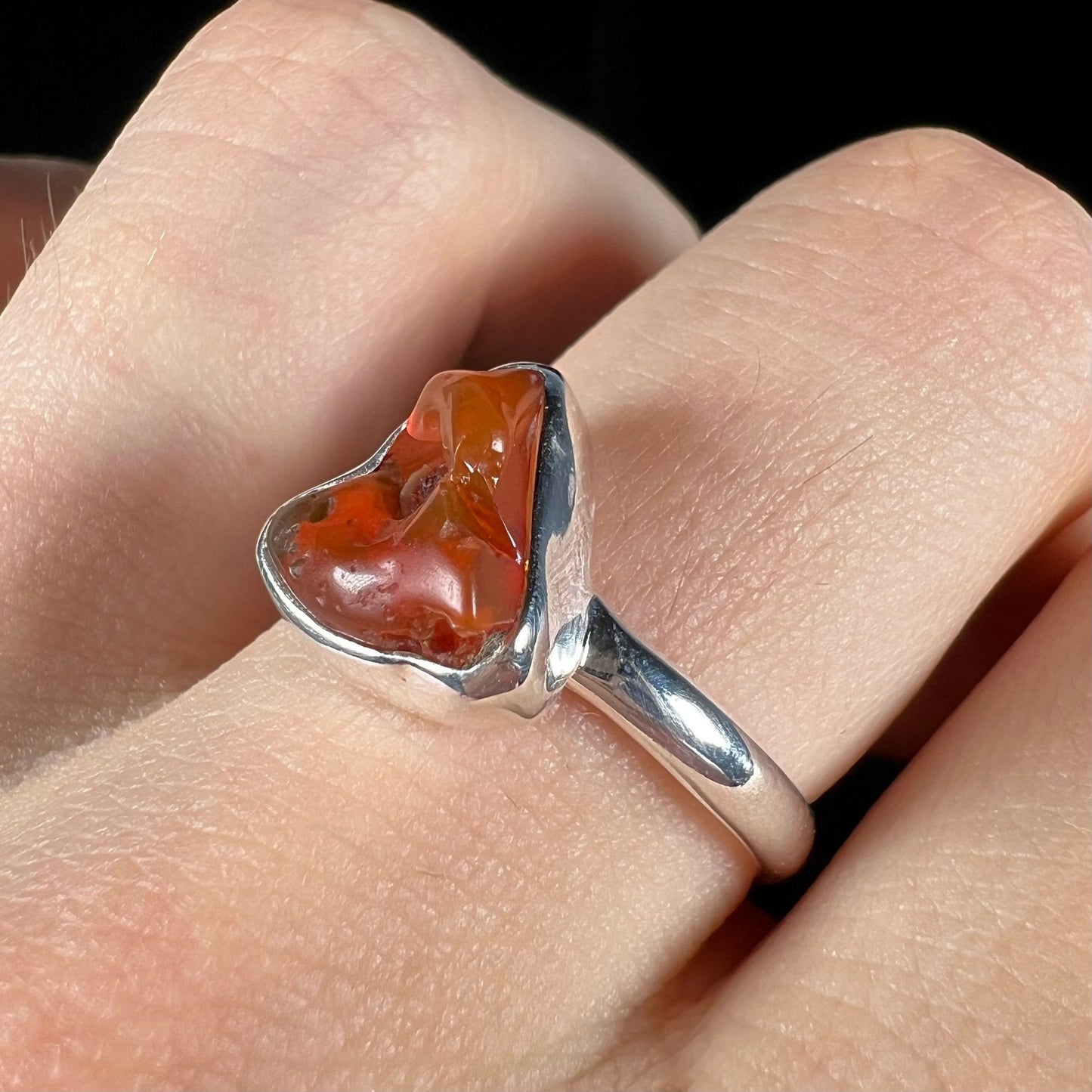 A polished fire opal crystal bezel set into a sterling silver ring. The opal is an orange color.