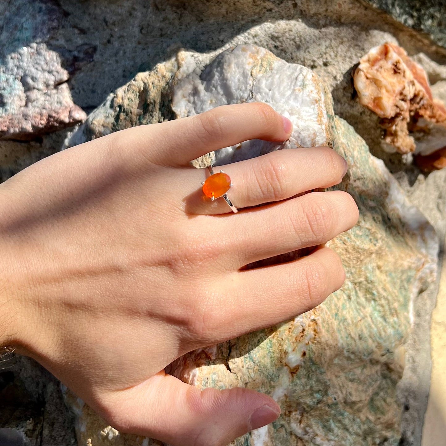 A silver solitaire ring set with a natural, faceted oval cut Mexican fire opal. The stone is a bright orange color.