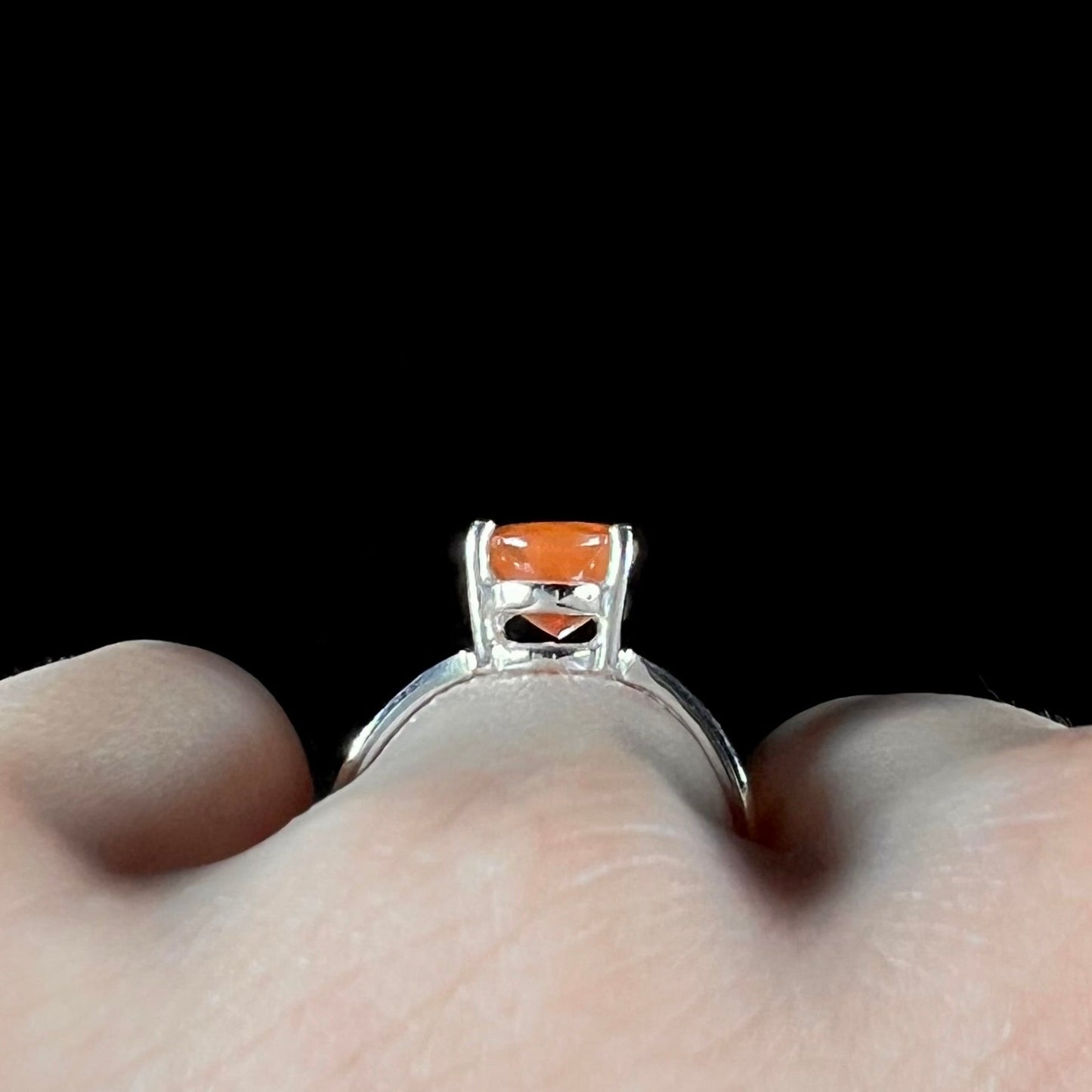 A silver solitaire ring set with a natural, faceted oval cut Mexican fire opal. The stone is a bright orange color.
