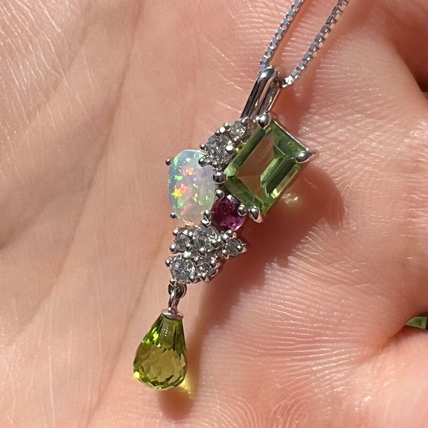 A multi-gemstone cluster pendant held in a hand at an angle in natural daylight.