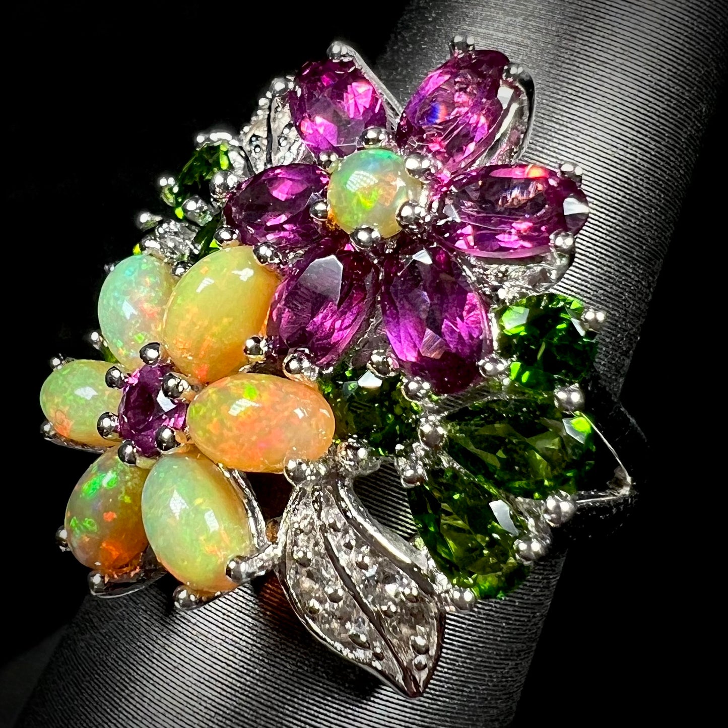 A multi-gemstone flower ring set with Ethiopian opals, rhodolite garnets, and chrome diopside, shown at an angle.