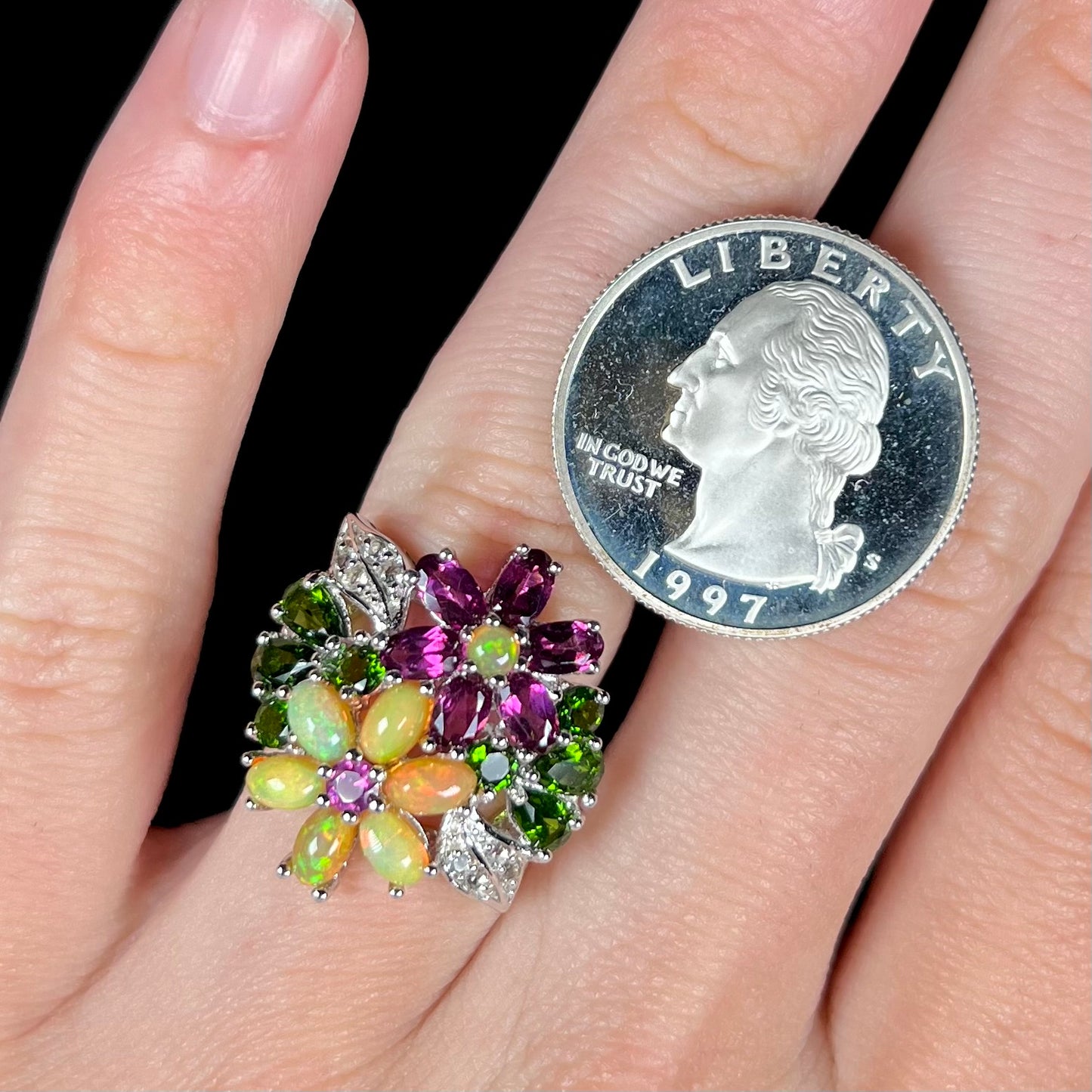 A multi-gemstone flower ring with Ethiopian opal, worn on a finger next to a 1997 quarter coin for scale.