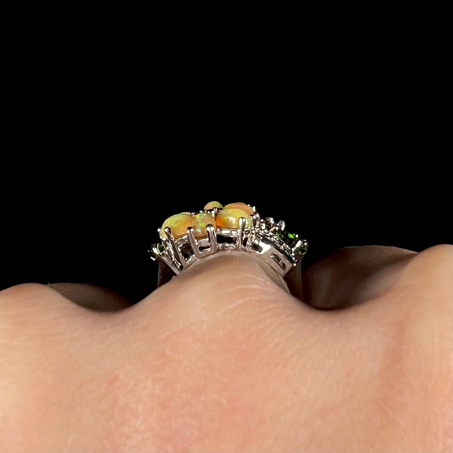 Side gallery view of a silver multi-gemstone ring, worn on a finger against a black background.