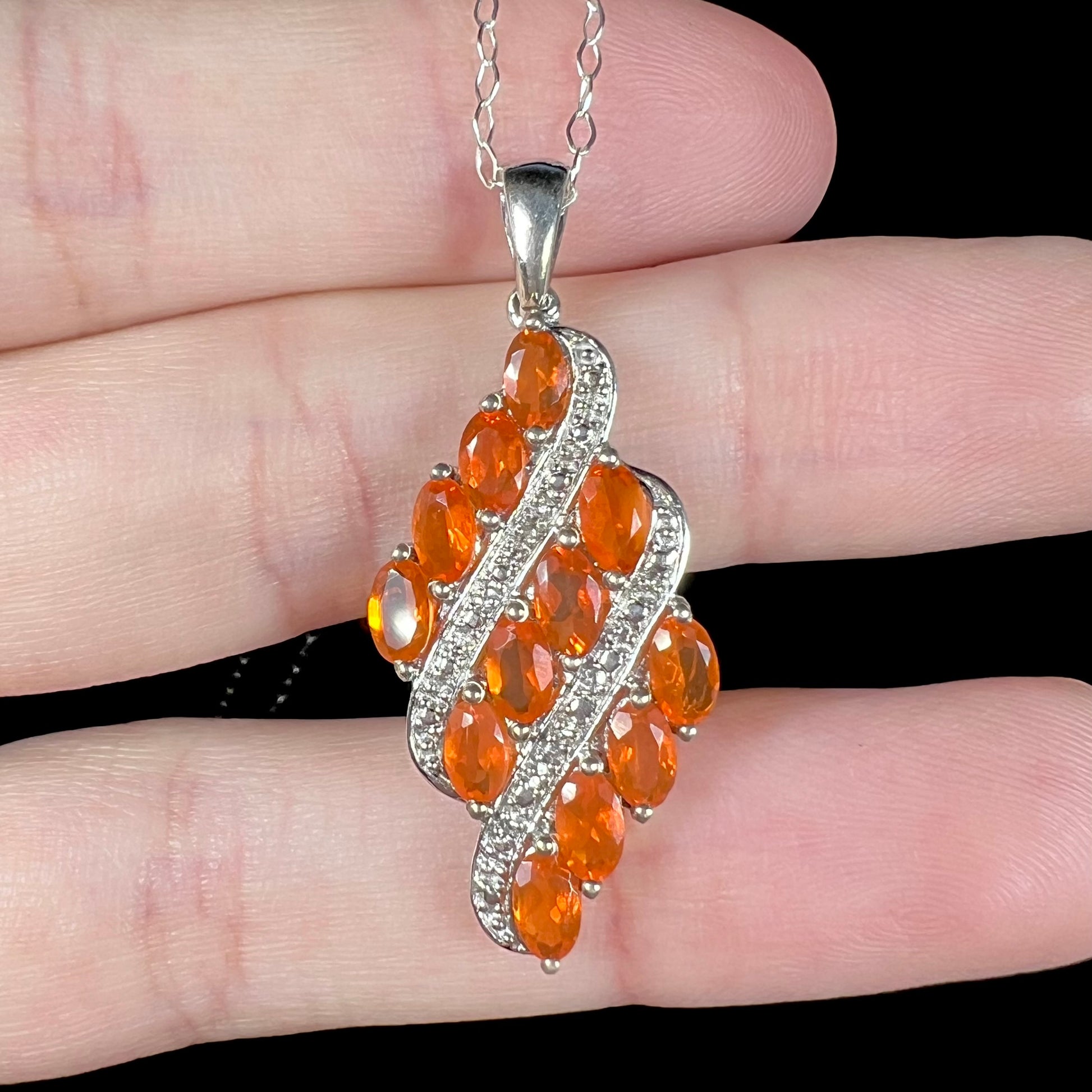 Close-up of a silver multistone fire opal necklace featuring a cluster of faceted orange fire opals in a hand.