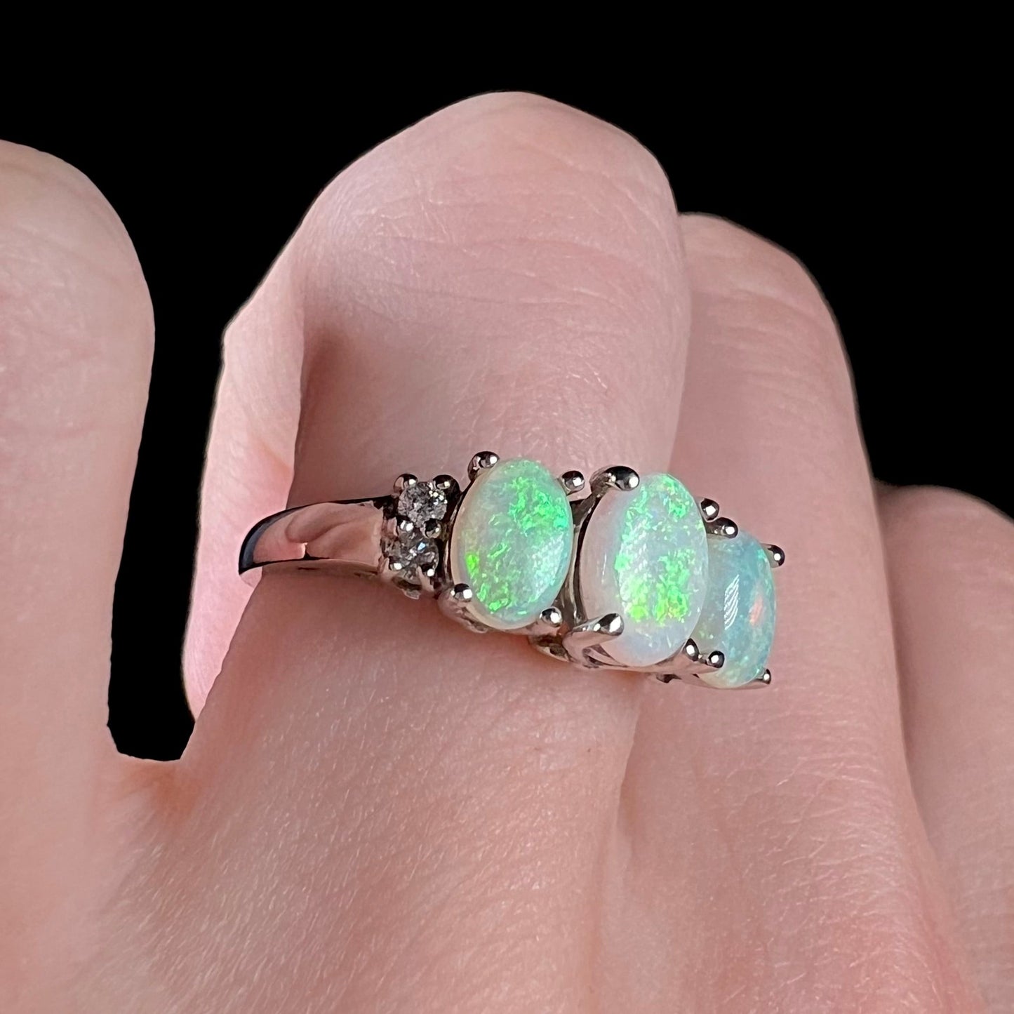 A ladies' white gold ring prong-set with three natural white opals and diamond accents. The opals play a green color.