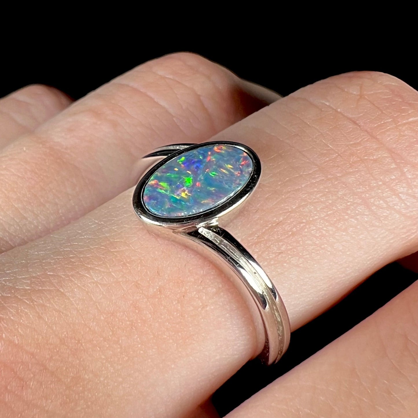 A sterling silver ring bezel-set with an oval shaped black opal doublet. The opal has red and blue fire.