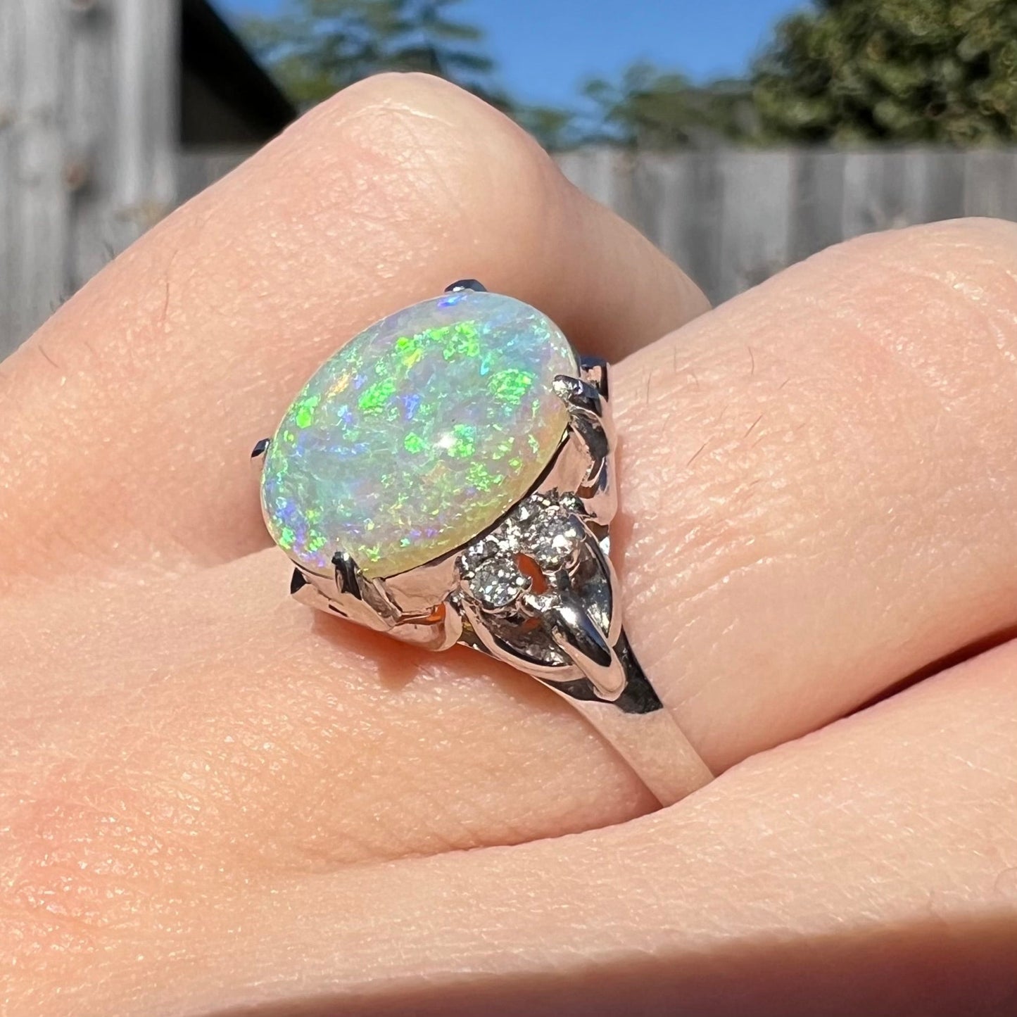 An Australian crystal opal engagement ring set with diamonds in a platinum filigree mounting. The opal plays green/blue colors and has a crack.