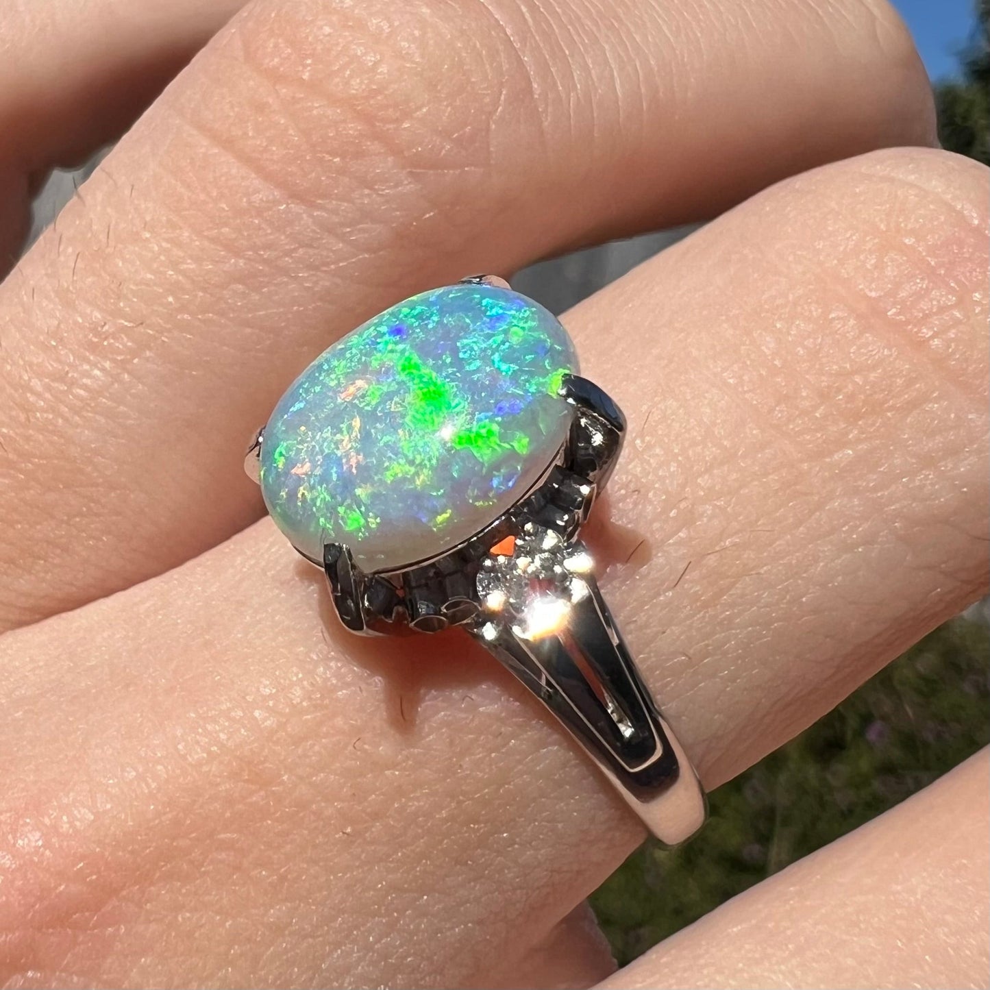 A platinum filigree opal engagement ring set with diamond accents. The opal has green-blue colors.