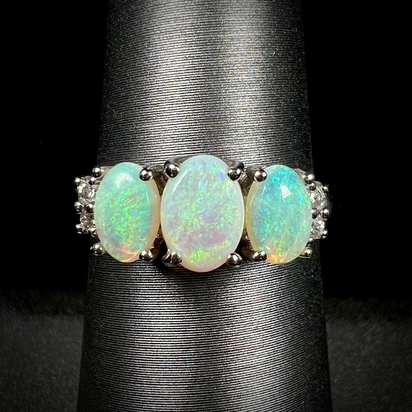 A ladies' white gold ring prong-set with three natural white opals and diamond accents. The opals play a green color.