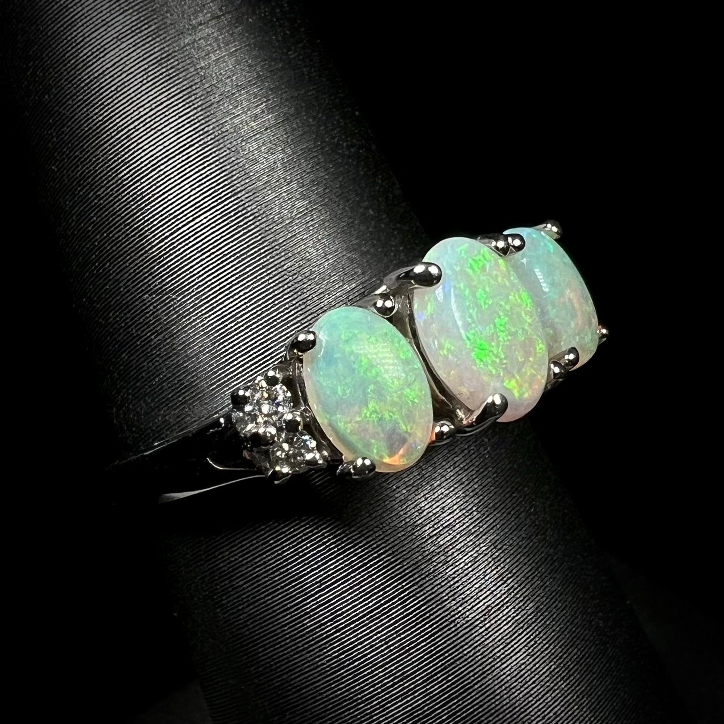 A ladies' white gold ring prong-set with three natural white opals and diamond accents. The opals play a green color.