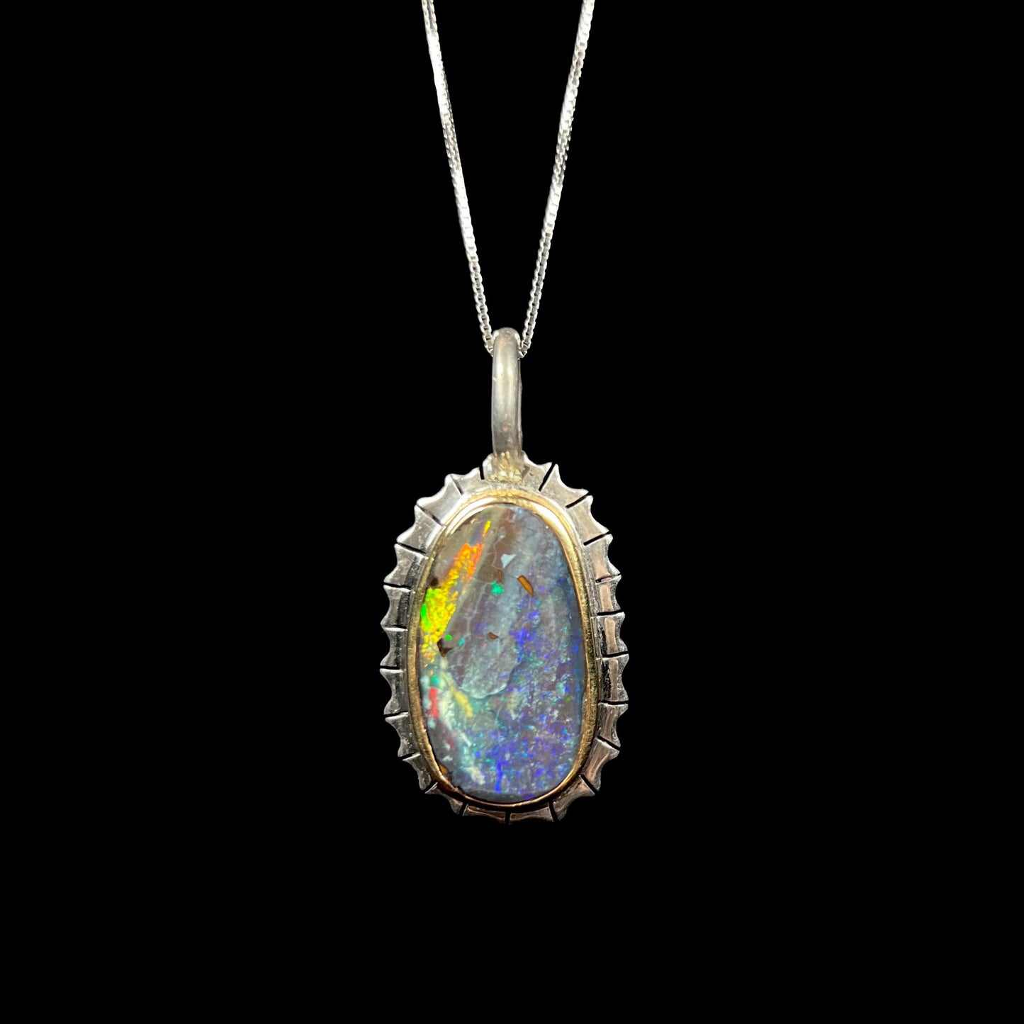 A Southwest style two-tone sterling silver pendant set with a black boulder opal with a yellow gold bezel.