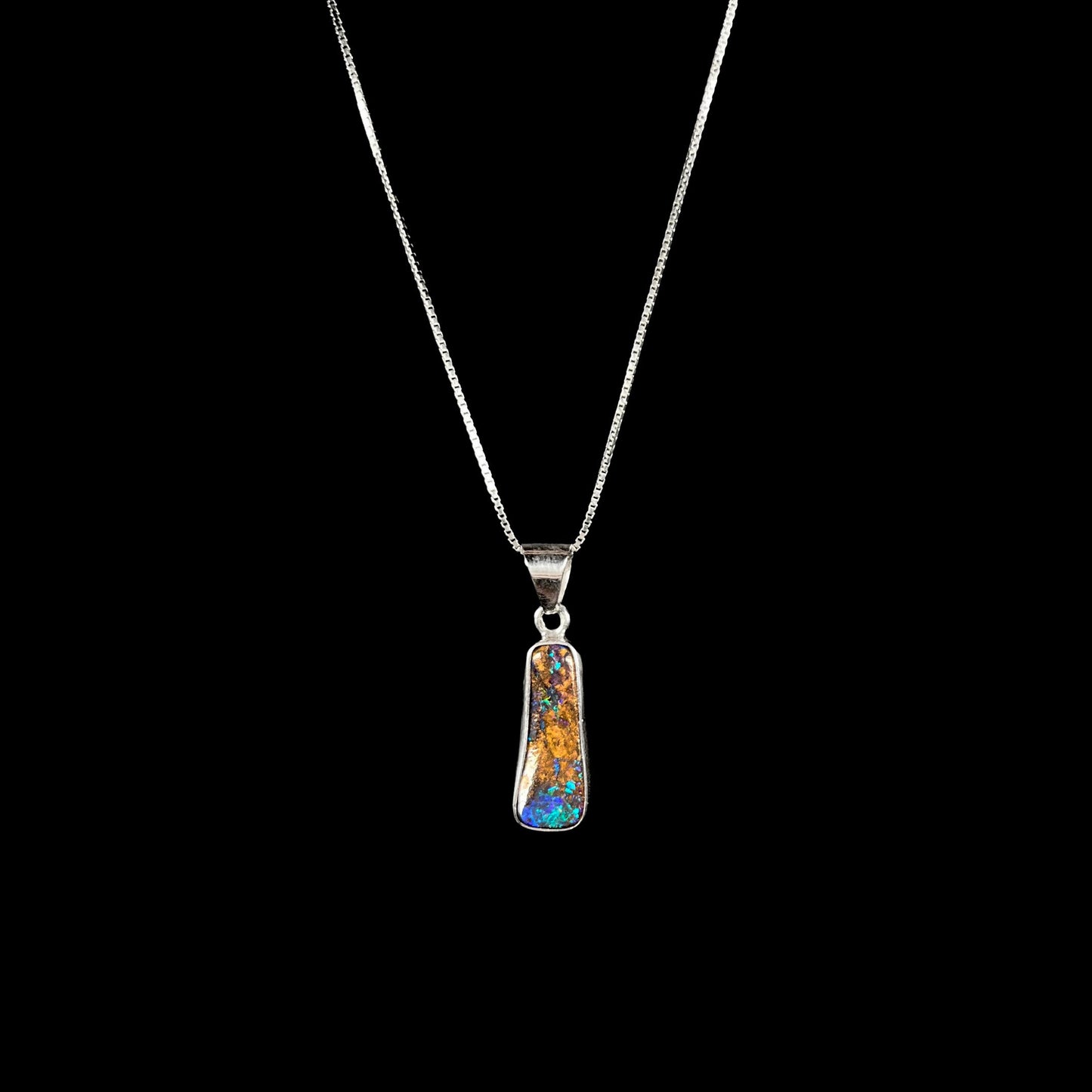 A sterling silver necklace bezel set with a natural Australian boulder opal stone. The stone shines colors of blue, green, and purple.