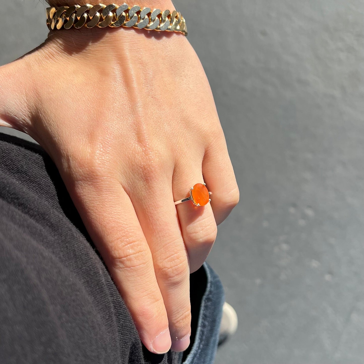 A silver solitaire ring set with a natural, faceted oval cut Mexican fire opal. The stone is a bright orange color.