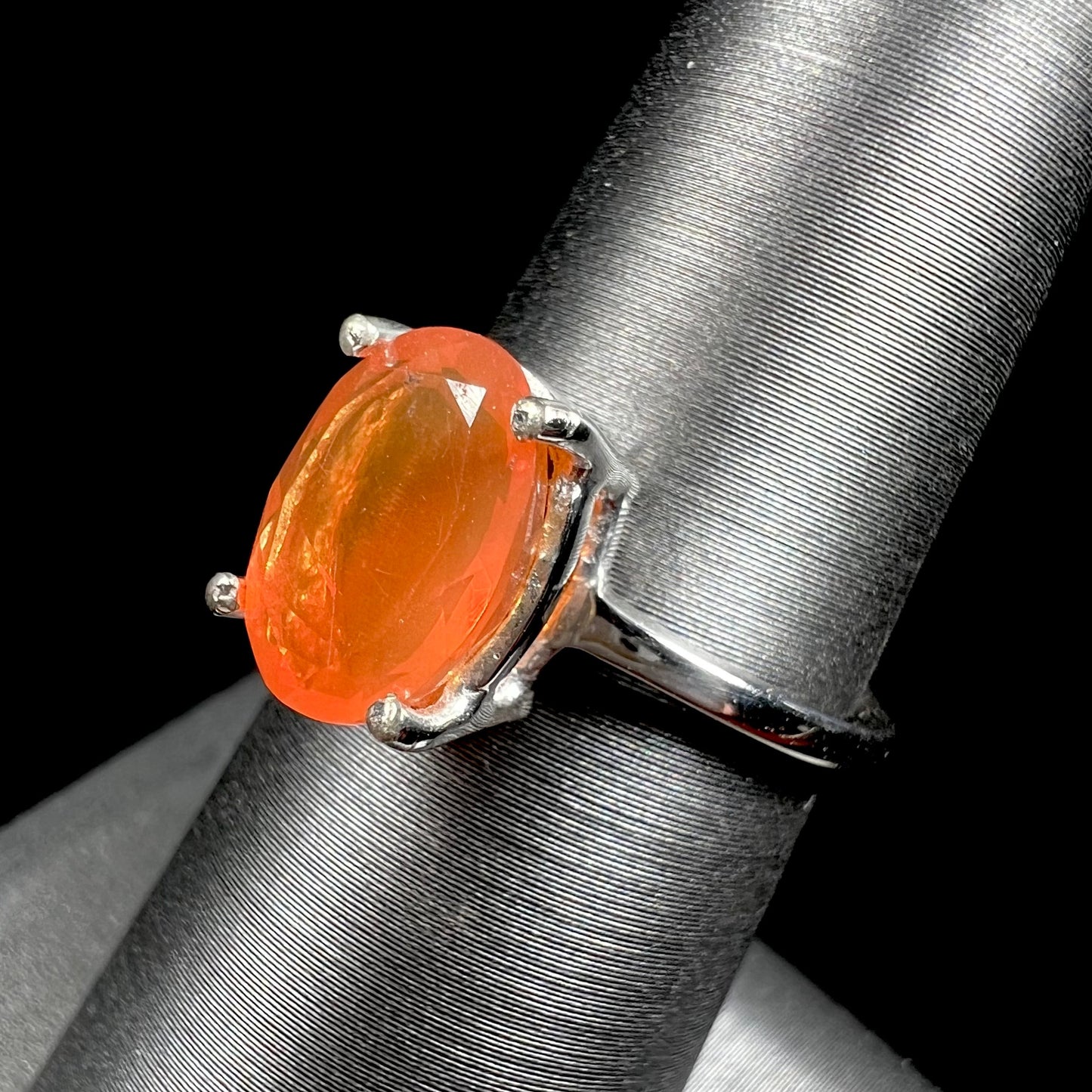 A silver solitaire ring set with a natural, faceted oval cut Mexican fire opal. The stone is a bright orange color.