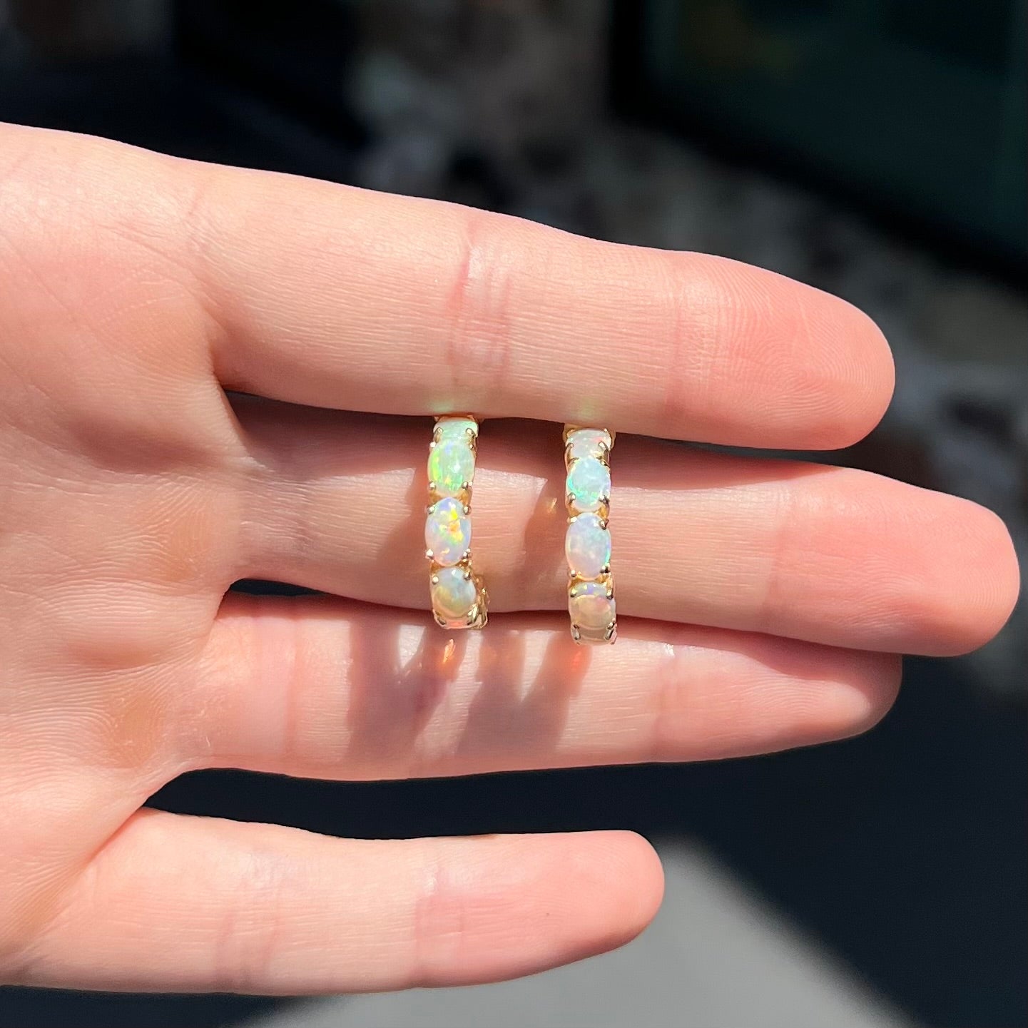 A pair of yellow gold opal hoop earrings. Each earring is set with six natural oval cut opals.