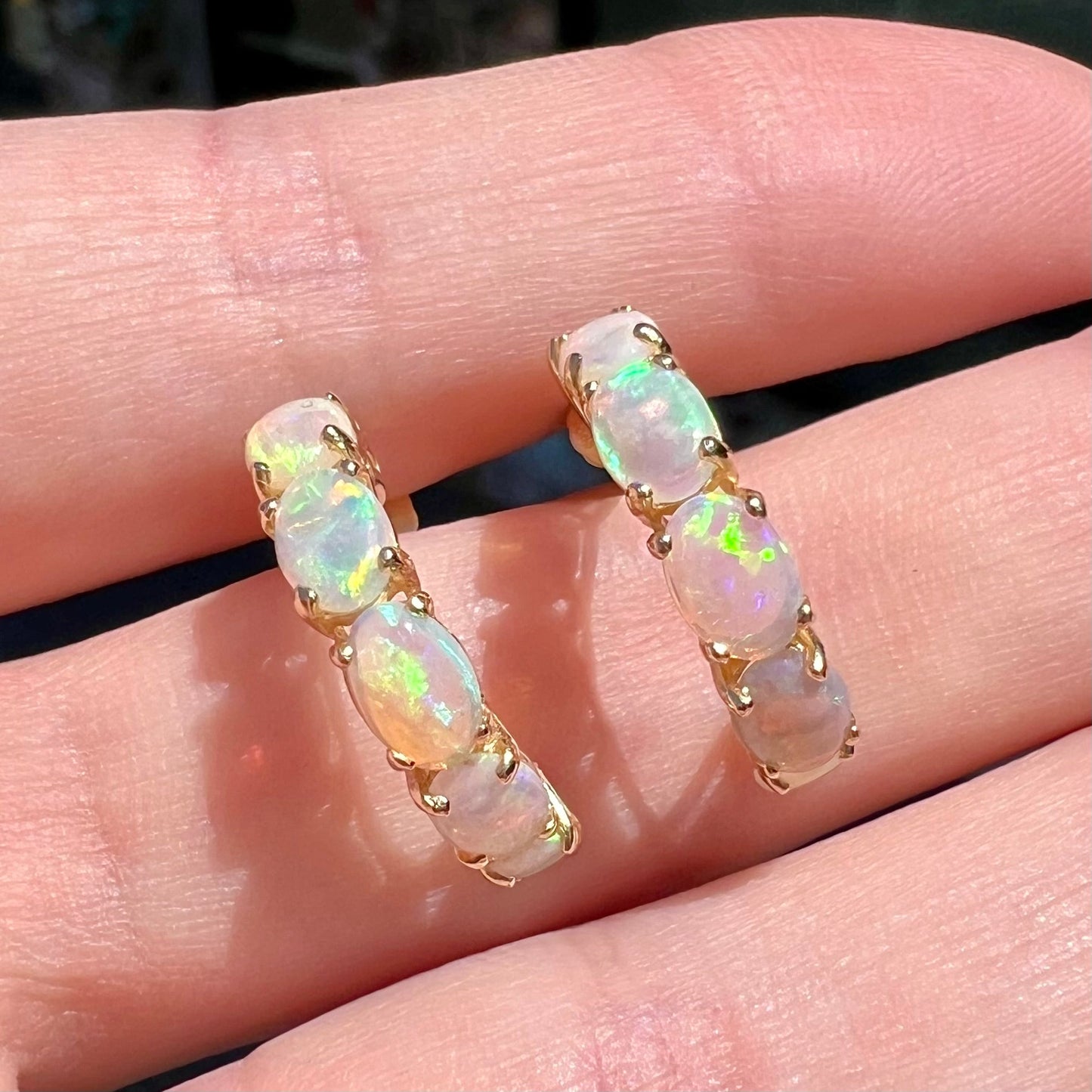 A pair of yellow gold opal hoop earrings. Each earring is set with six natural oval cut opals.