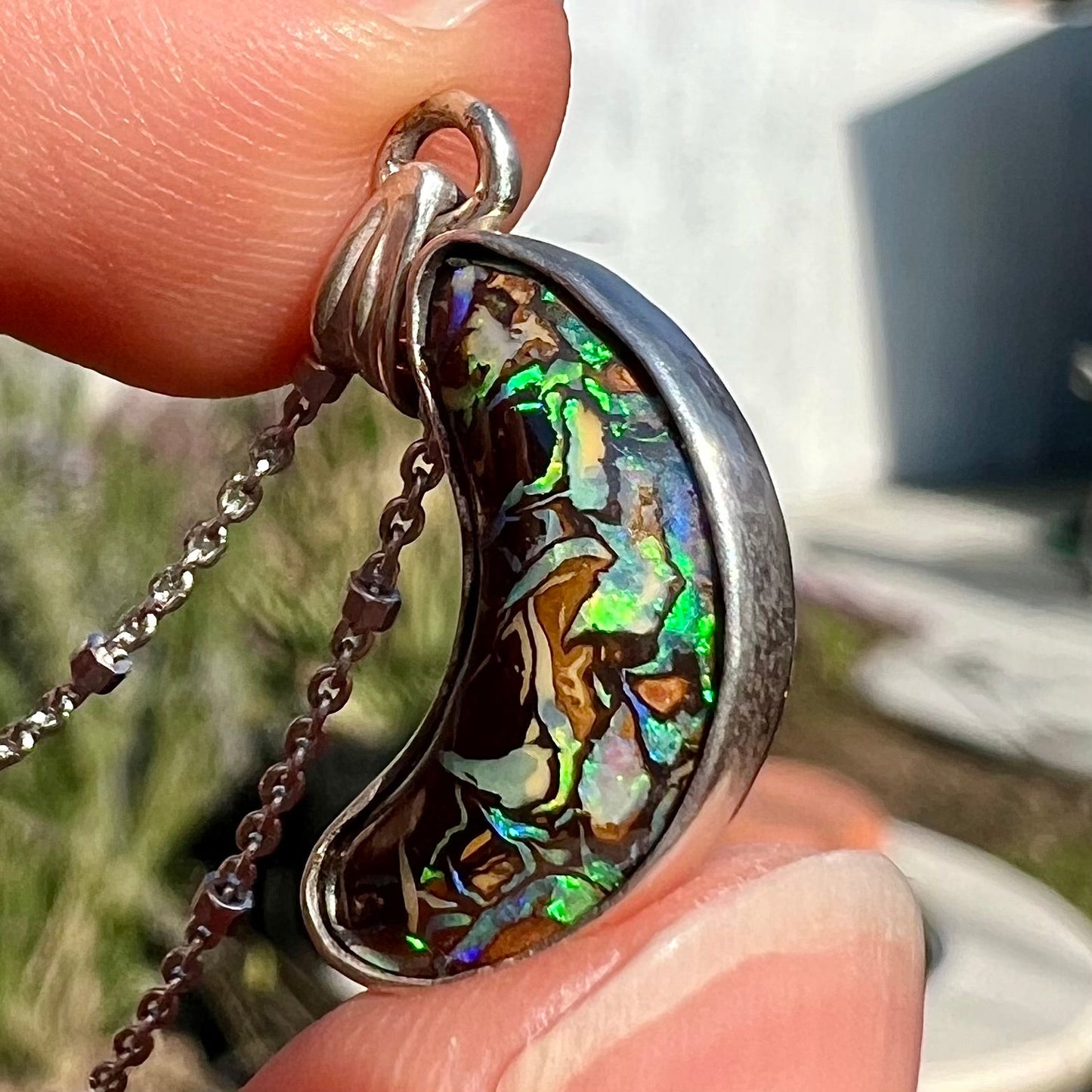 A sterling silver necklace set with a natural Koroit boulder opal shaped like a crescent moon.