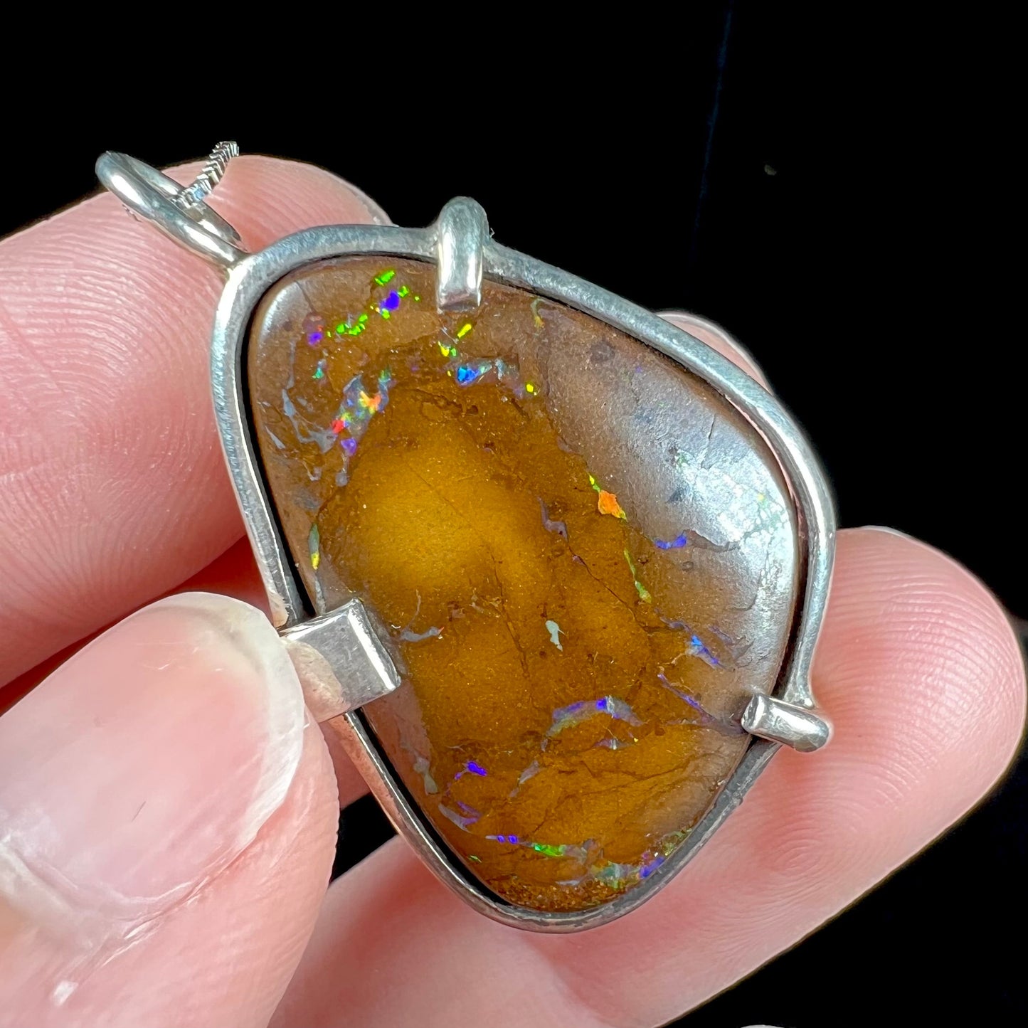 A handmade sterling silver pendant bezel and prong set with a natural boulder opal stone. The opal shines veins of color.