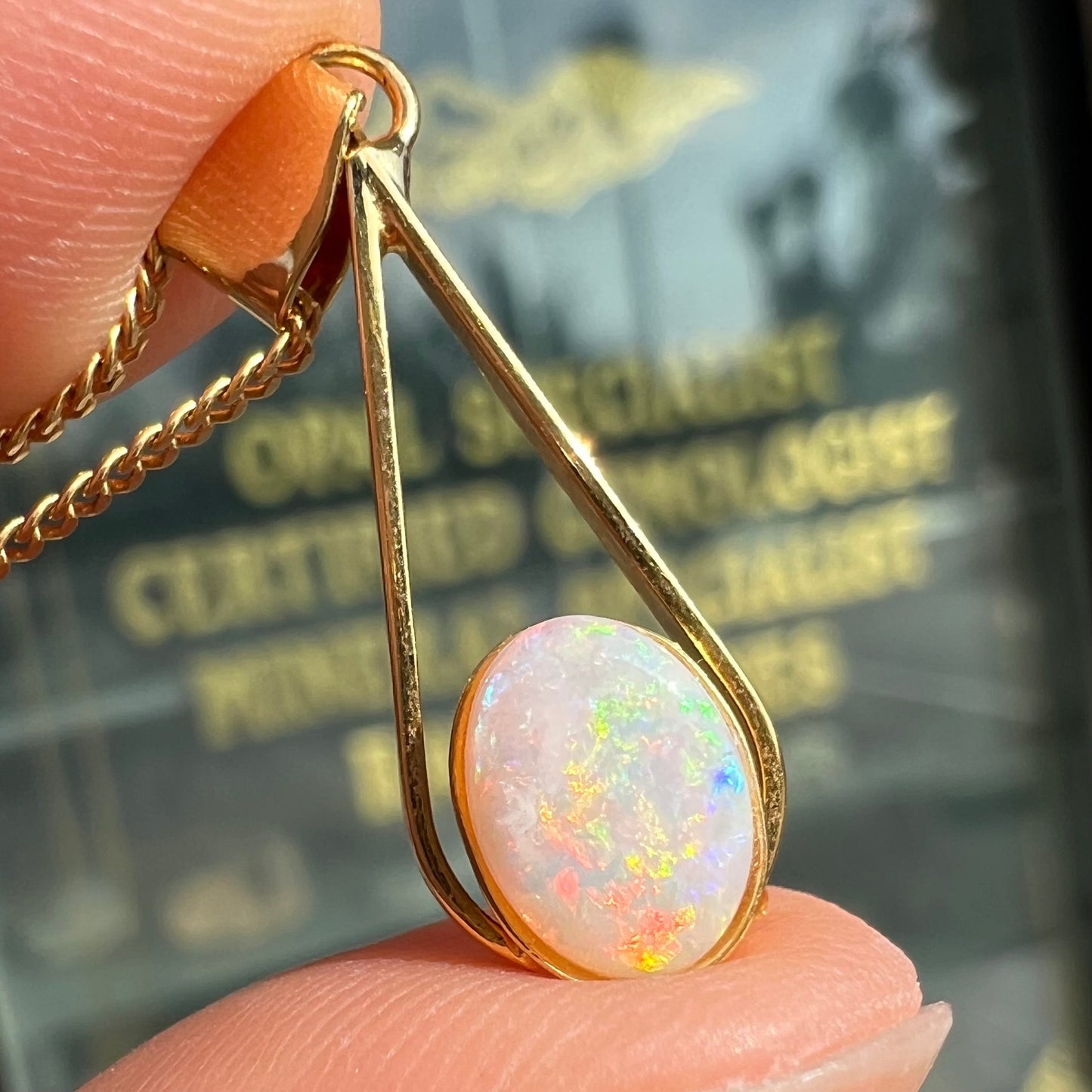 A gold plated necklace set with a natural white crystal opal. The opal shines pinkish red and blue colors.