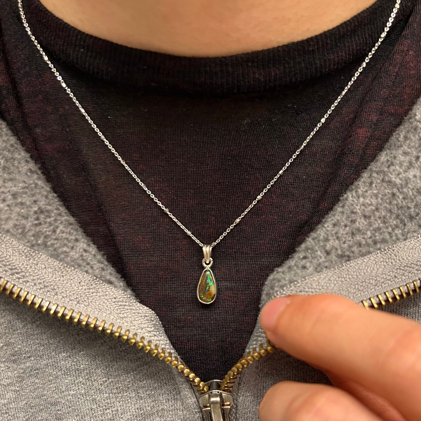 A natural, pear shaped Australian boulder opal with blue, purple, and green colors bezel set into a sterling silver necklace.