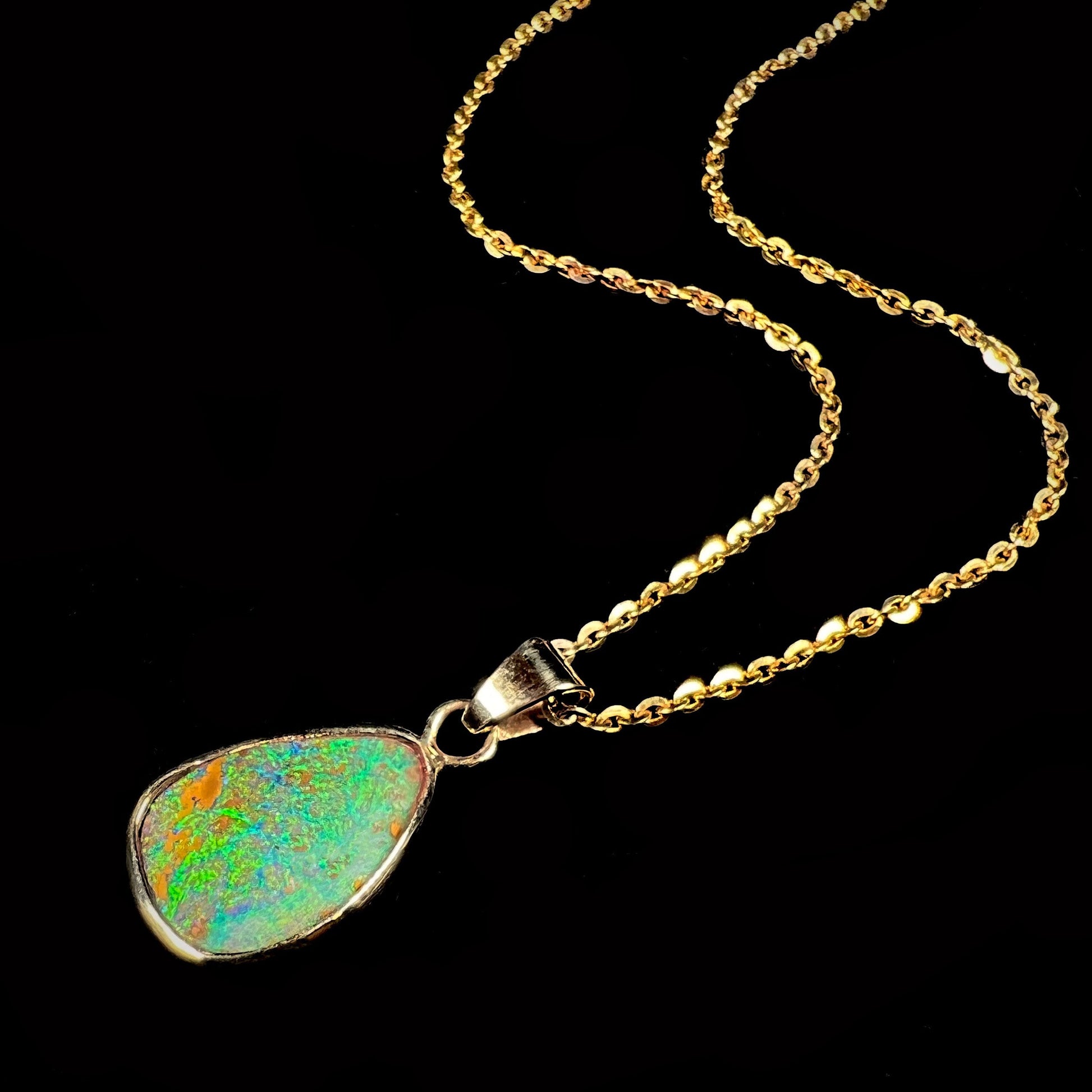 A ladies' natural boulder opal necklace set in 14k yellow gold.  The opal is bezel set and shows green and blue colors.