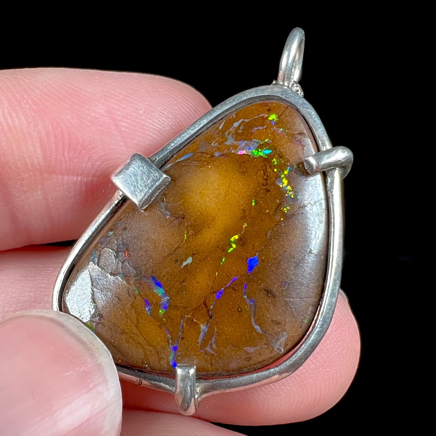 A handmade sterling silver pendant bezel and prong set with a natural boulder opal stone. The opal shines veins of color.