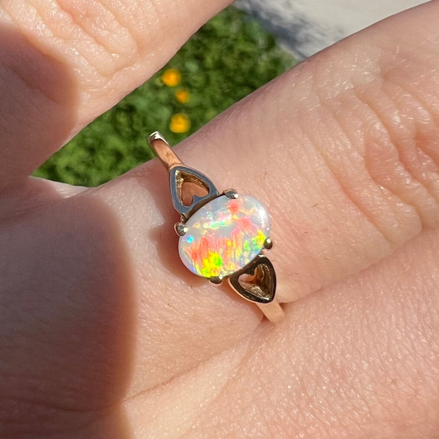 A dainty yellow gold ring mounted with a vivdly bright red Australian opal. The ring has two heart shaped designs.