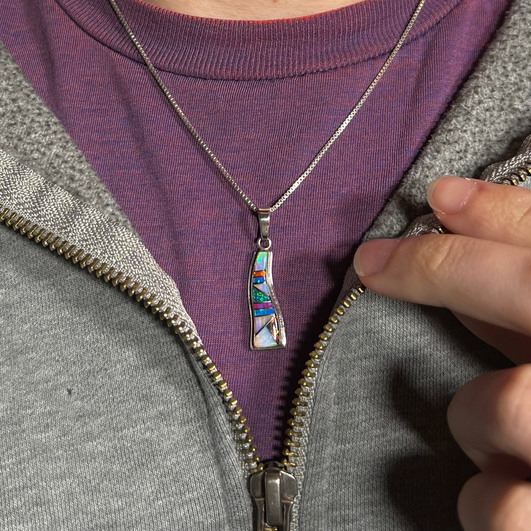 A Navajo-made silver opal inlay necklace worn around a neck against a purple shirt.