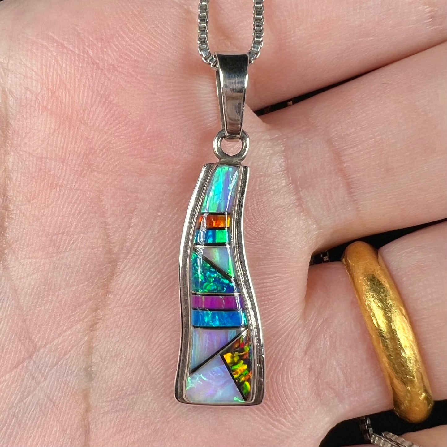 Close-up of a Navajo opal inlay pendant made from sterling silver, held in a hand.