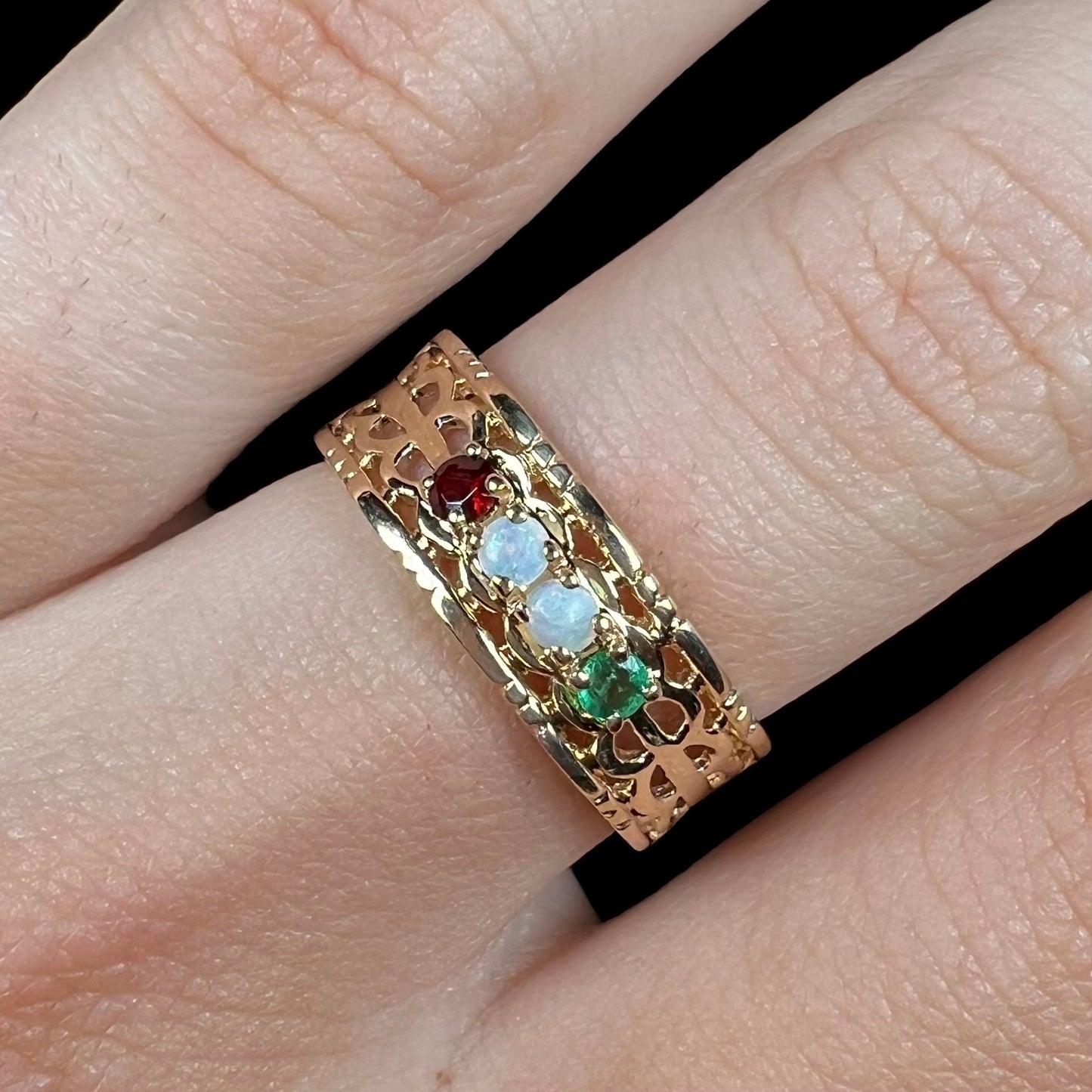 Close-up of a gold woven-style mother's ring set with two opals, an emerald, and a garnet worn on a finger.