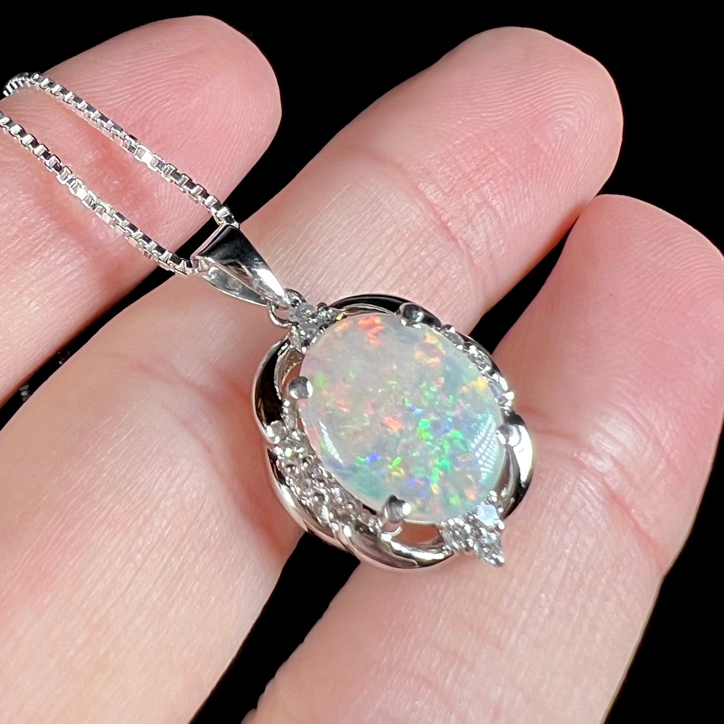 A platinum opal and diamond necklace held in a hand, shown at an angled view close-up.