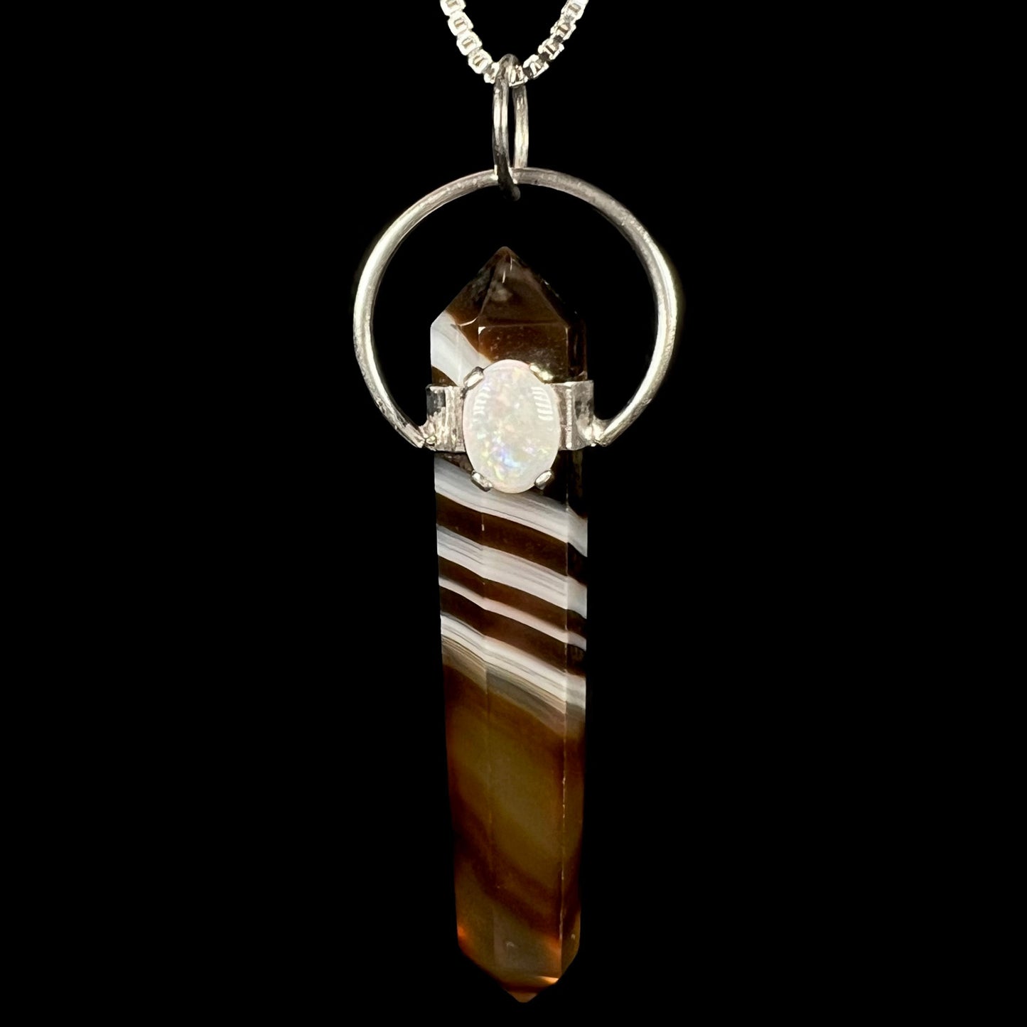 An opal and sardonyx crystal pendulum pendant shown from the front against a black background.