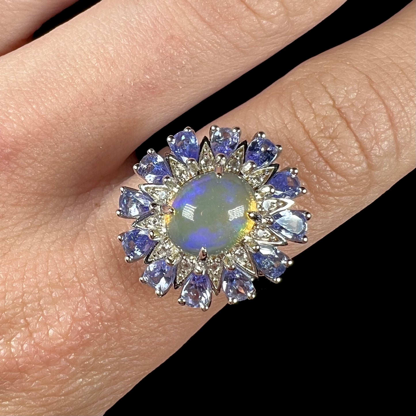 A blue Ethiopian opal and tanzanite ring, shown close-up from the front worn on a finger.