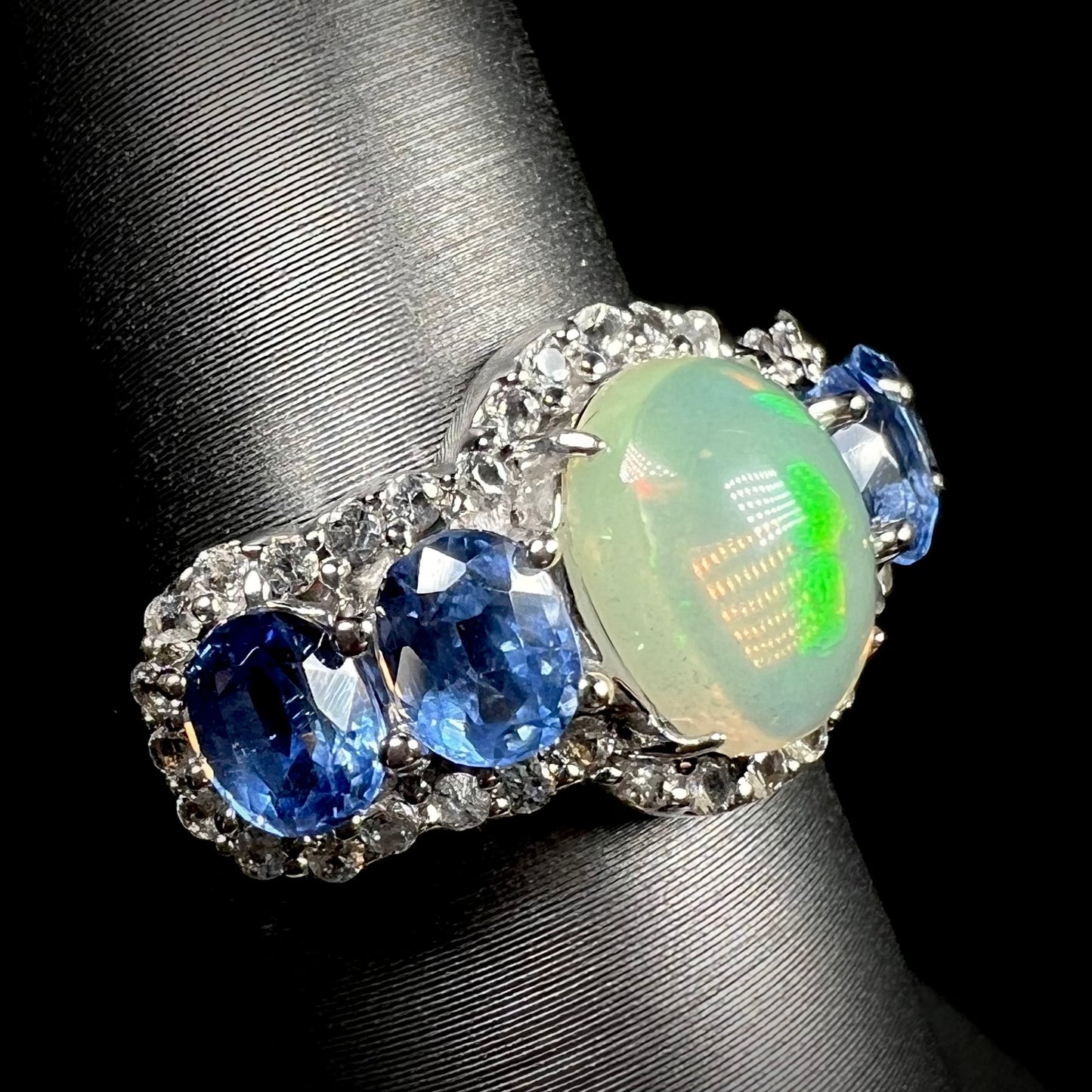 A sterling silver opal and blue kyanite gemstone ring shown at an angle against a black background.