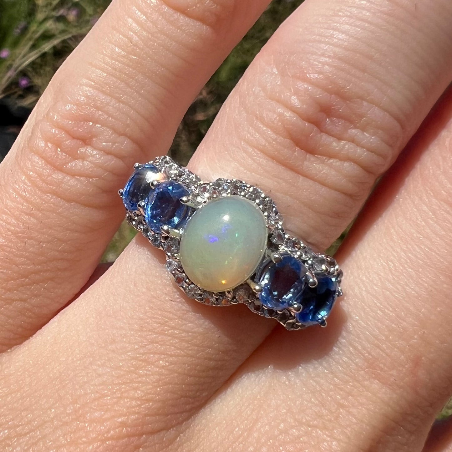 Close-up of sterling silver Ethiopian opal and kyanite ring worn on a hand in the sunlight.