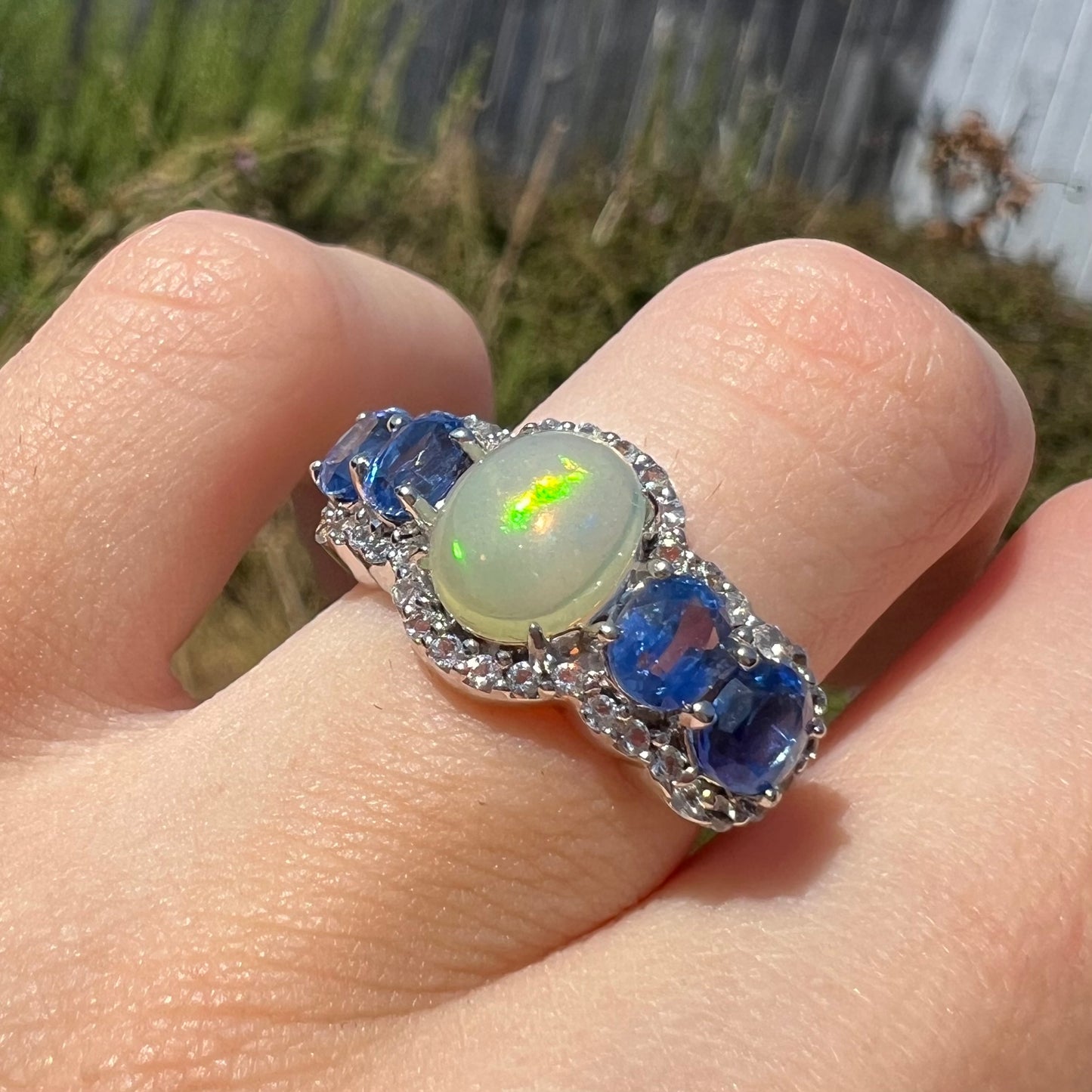 Close-up of sterling silver Ethiopian opal and kyanite ring worn on a hand in the sunlight.