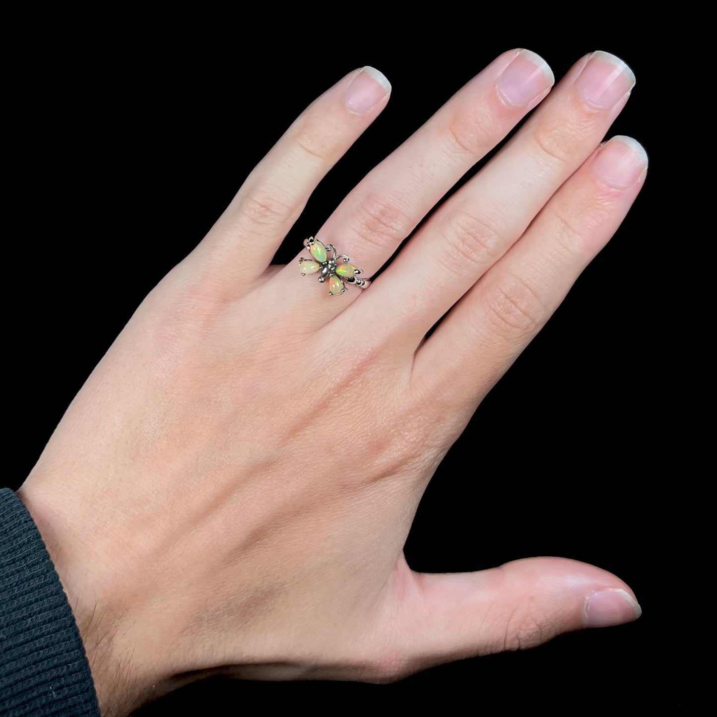 A sterling silver Ethiopian opal butterfly ring shown on a hand against a black background.