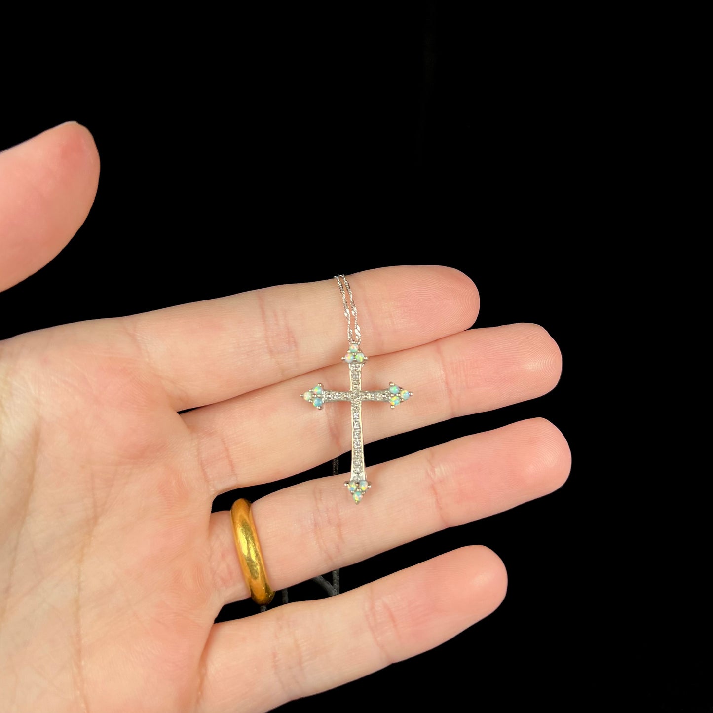 An opal cross necklace held in a hand against a black background.