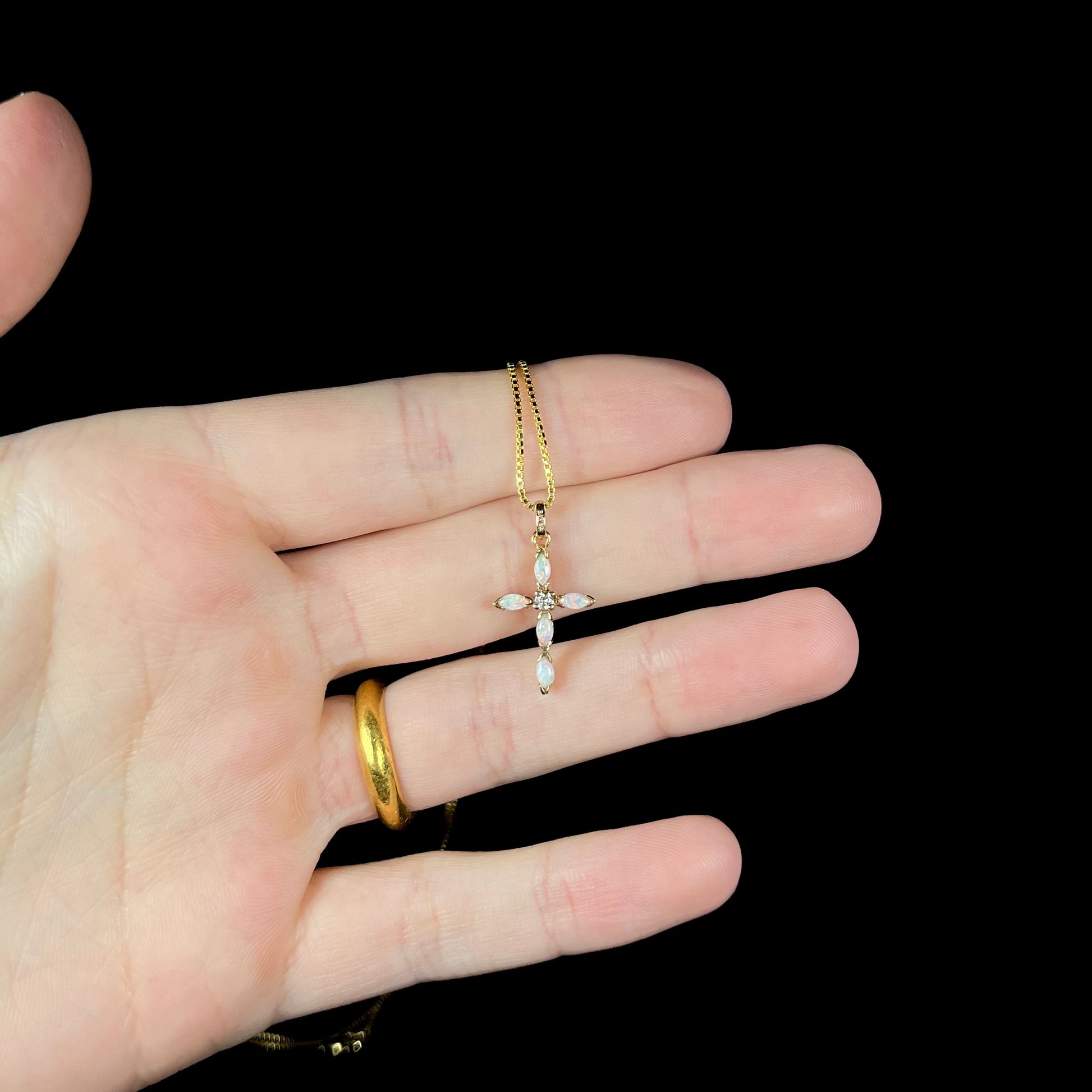 An opal cross necklace, held in a hand against a black background.