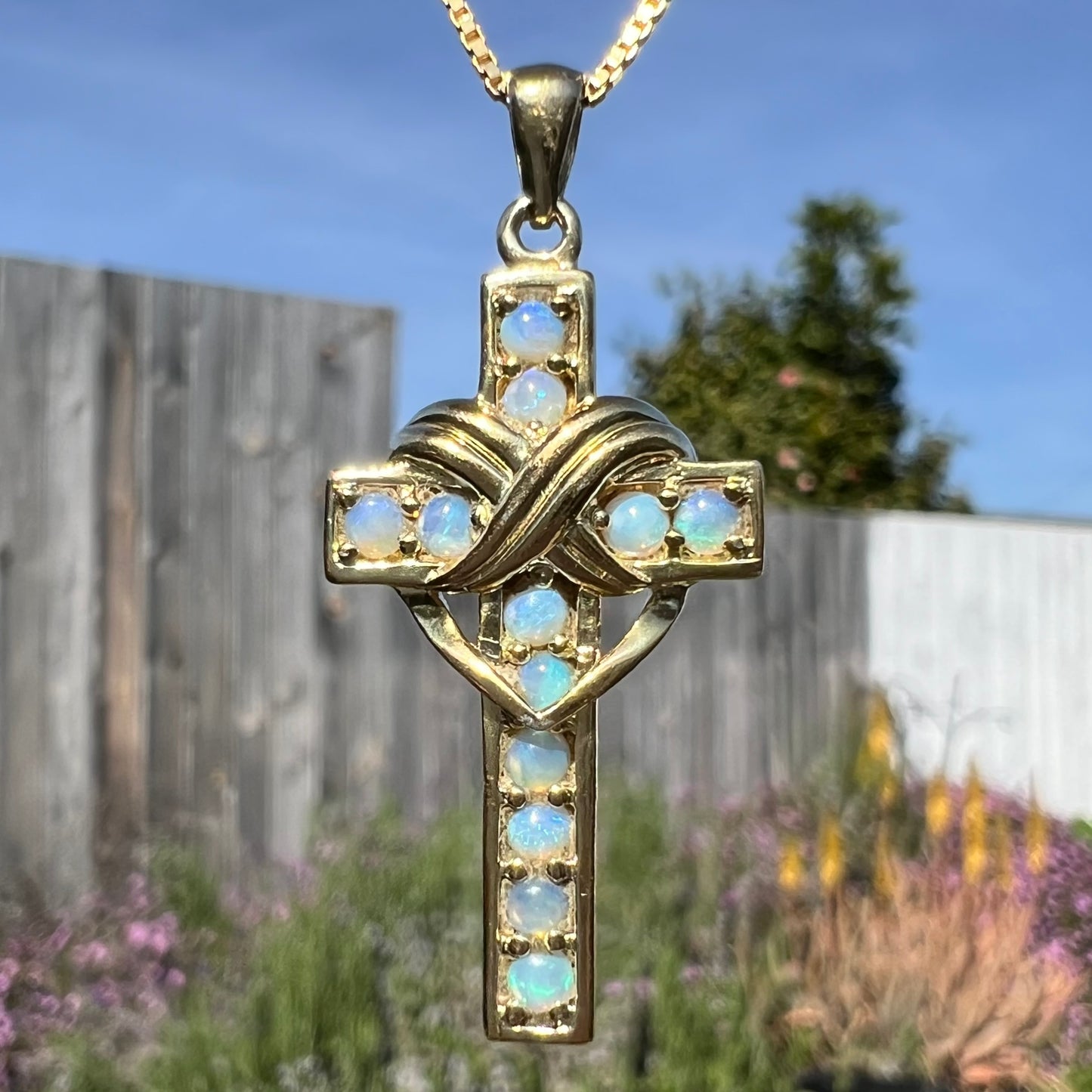 Macro sunlight view of gold-tone opal cross showing crystal opals.