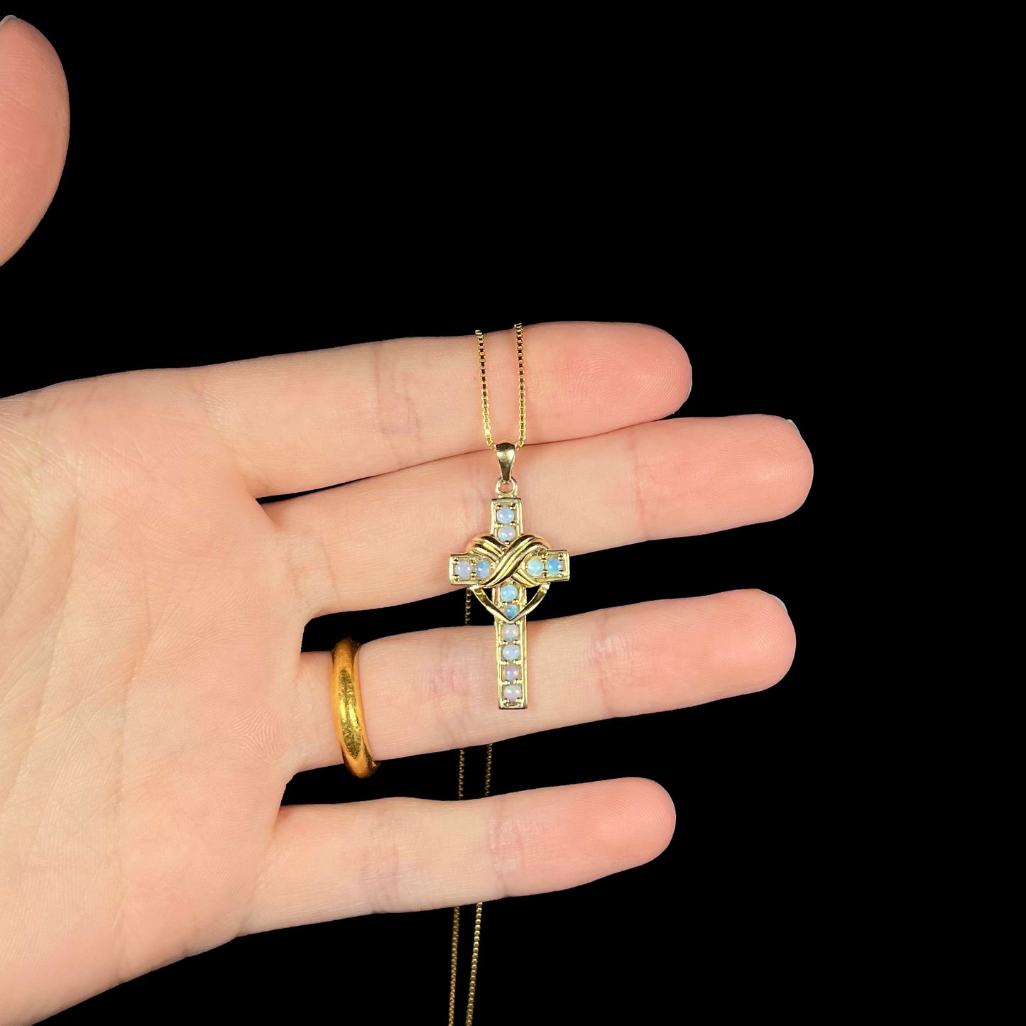 Cross necklace with crystal opals resting on fingers.