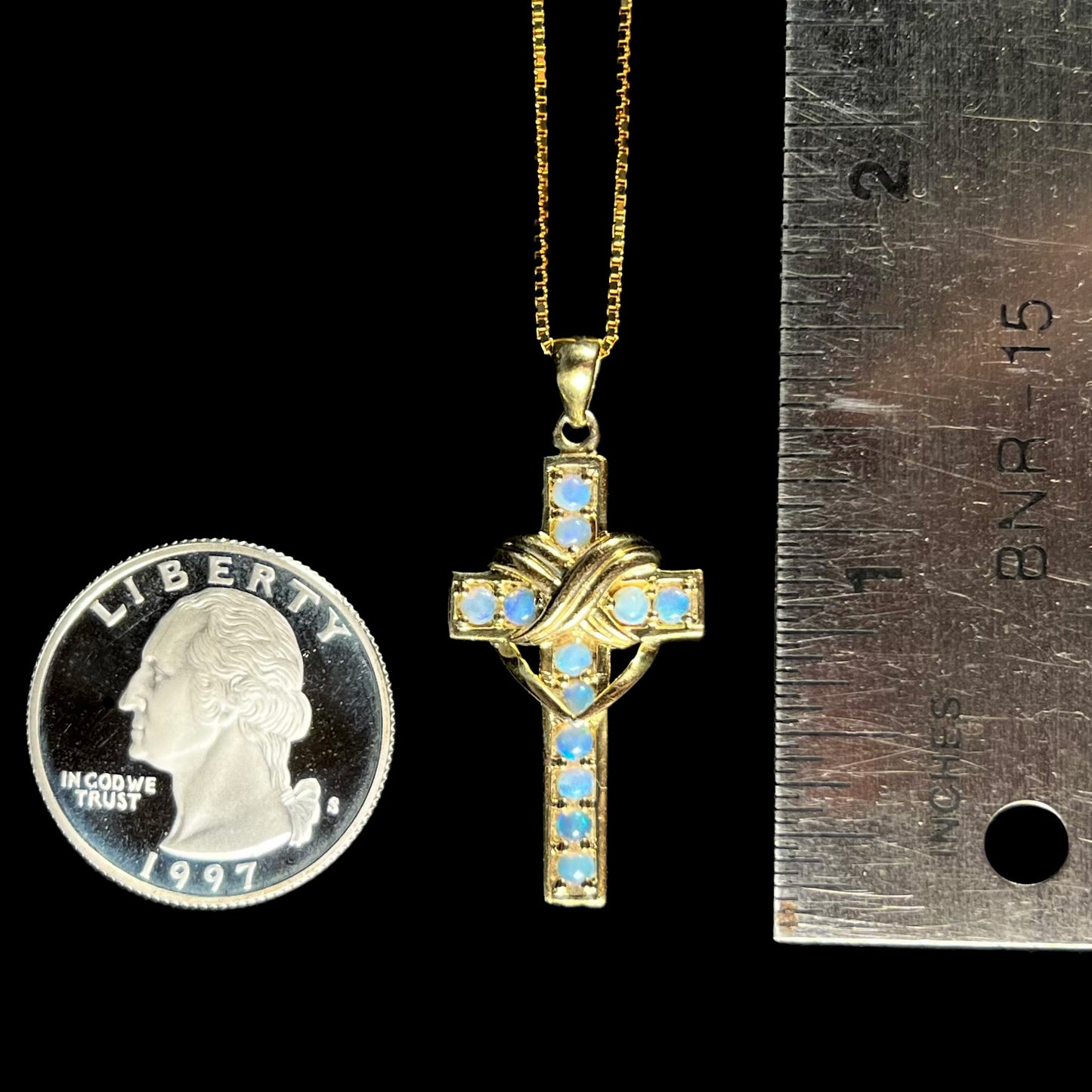 Opal cross pendant next to quarter and ruler for scale, about 1.5 inches long.