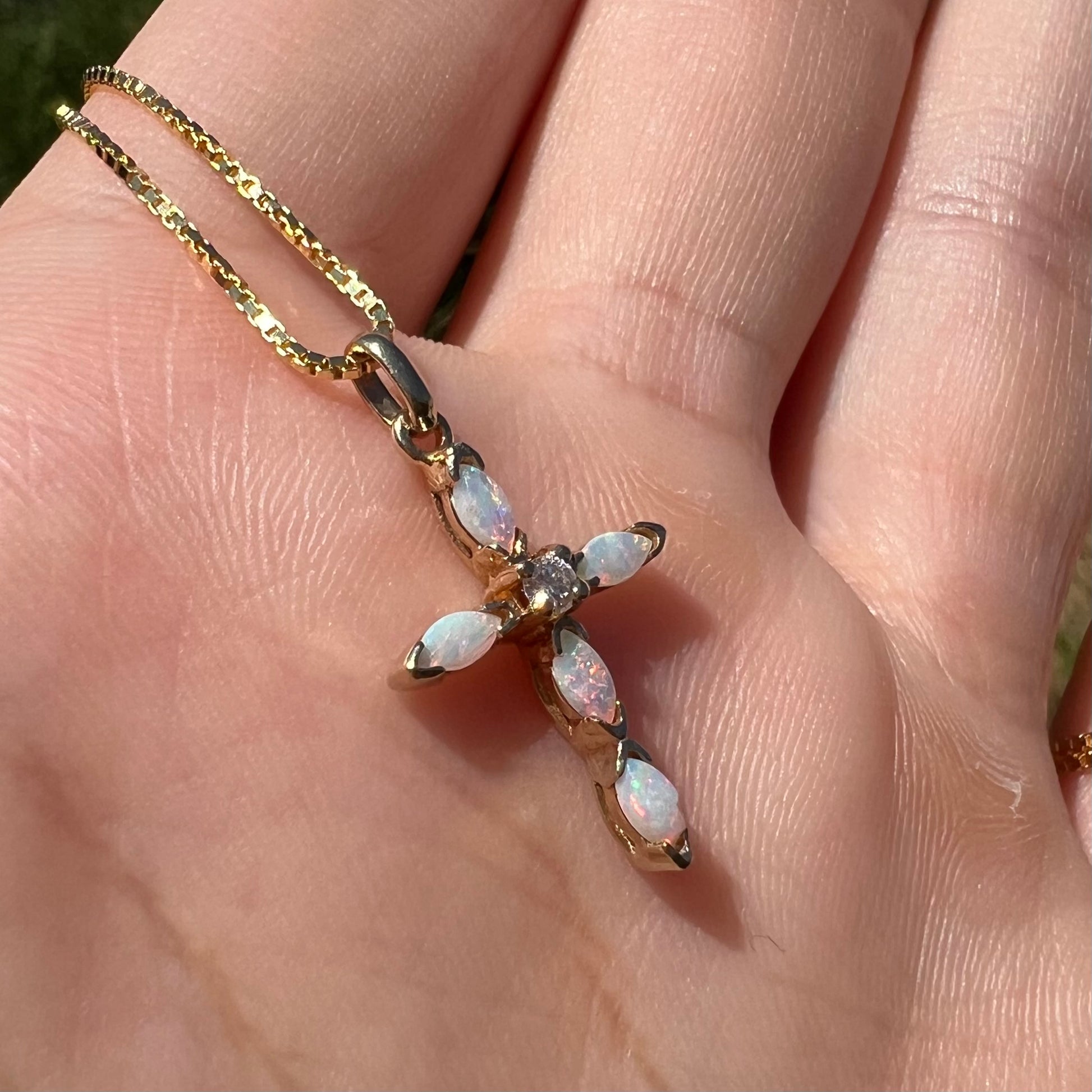 An opal cross necklace shown at an angle in the sunlight.