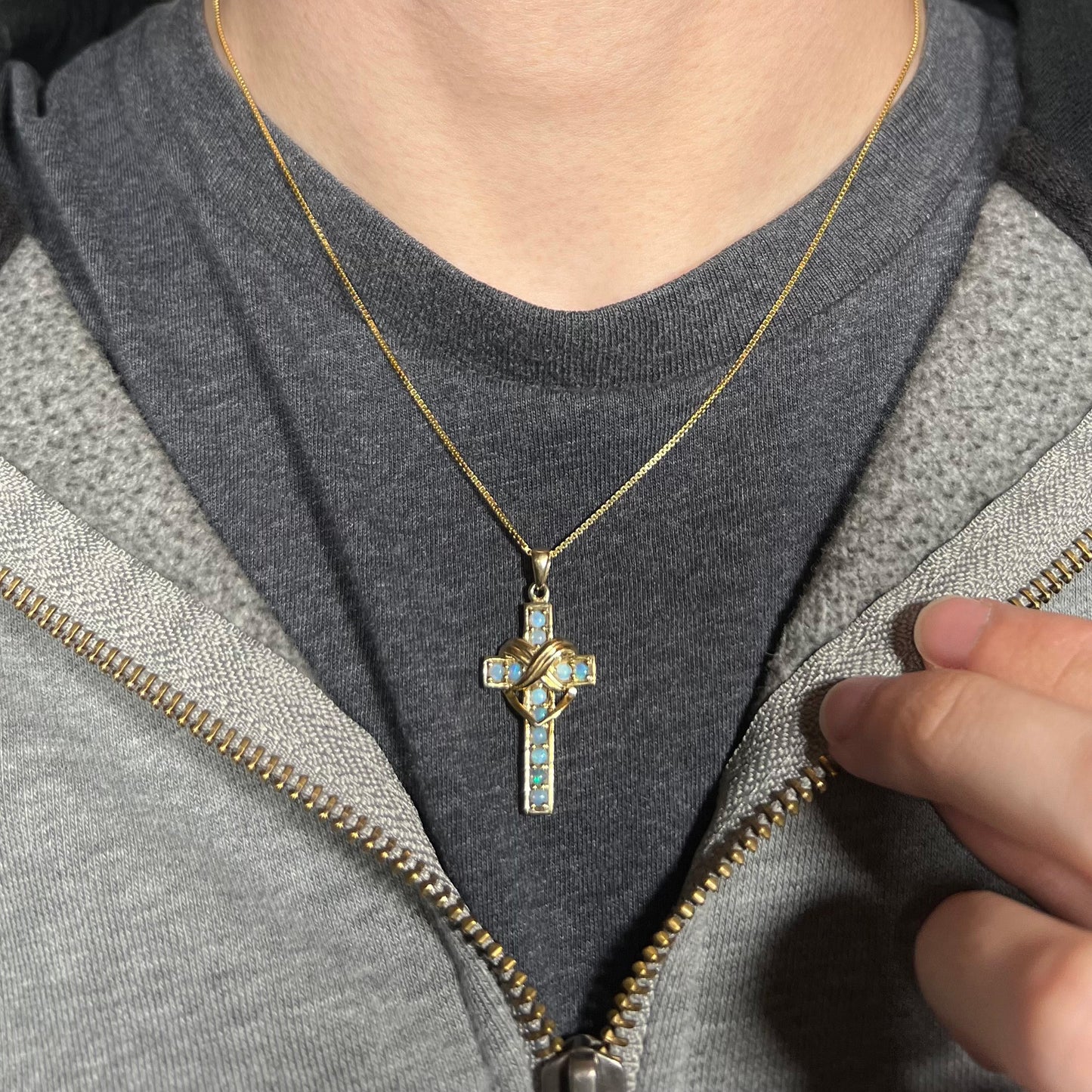 Opal cross necklace worn on black shirt with partially zipped sweatshirt.