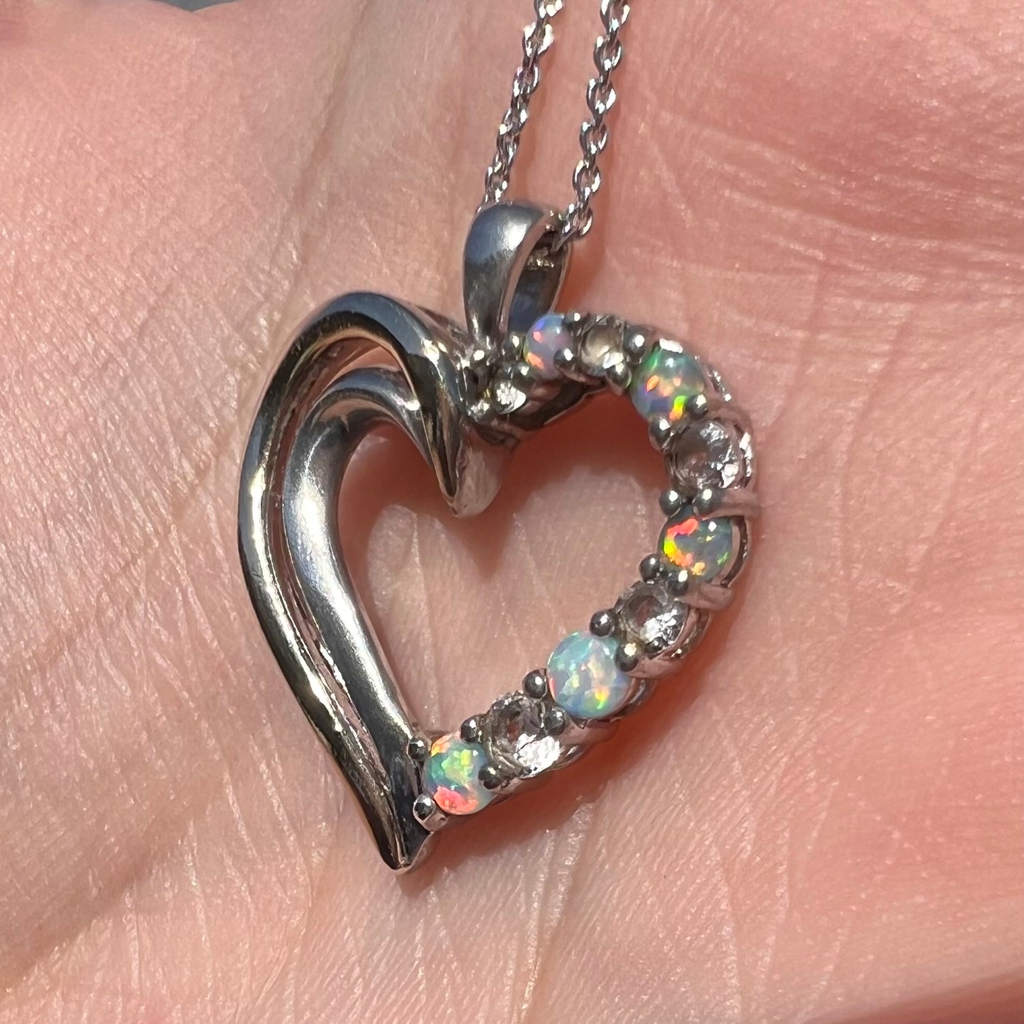 A two-tone sterling silver and yellow gold lab-created opal and CZ heart necklace shown in sunlight at an angle.