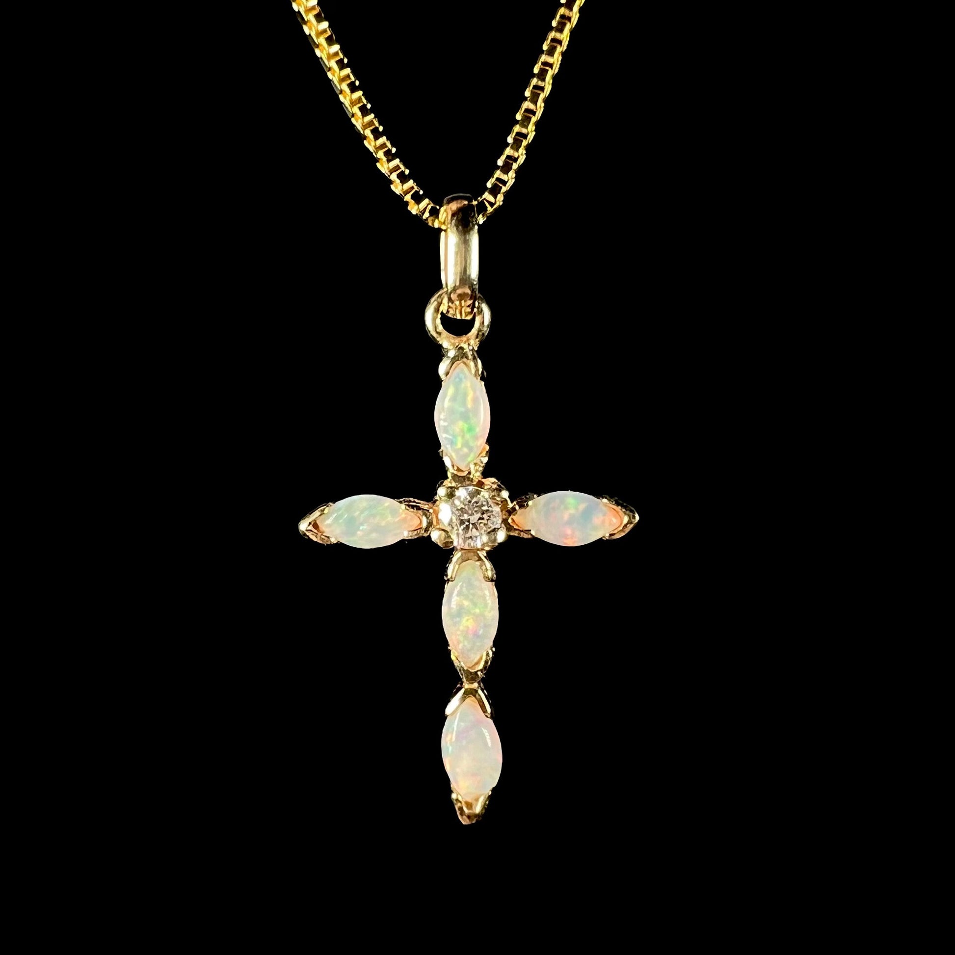 An opal and diamond cross necklace in yellow gold, shown from the front against a black background.