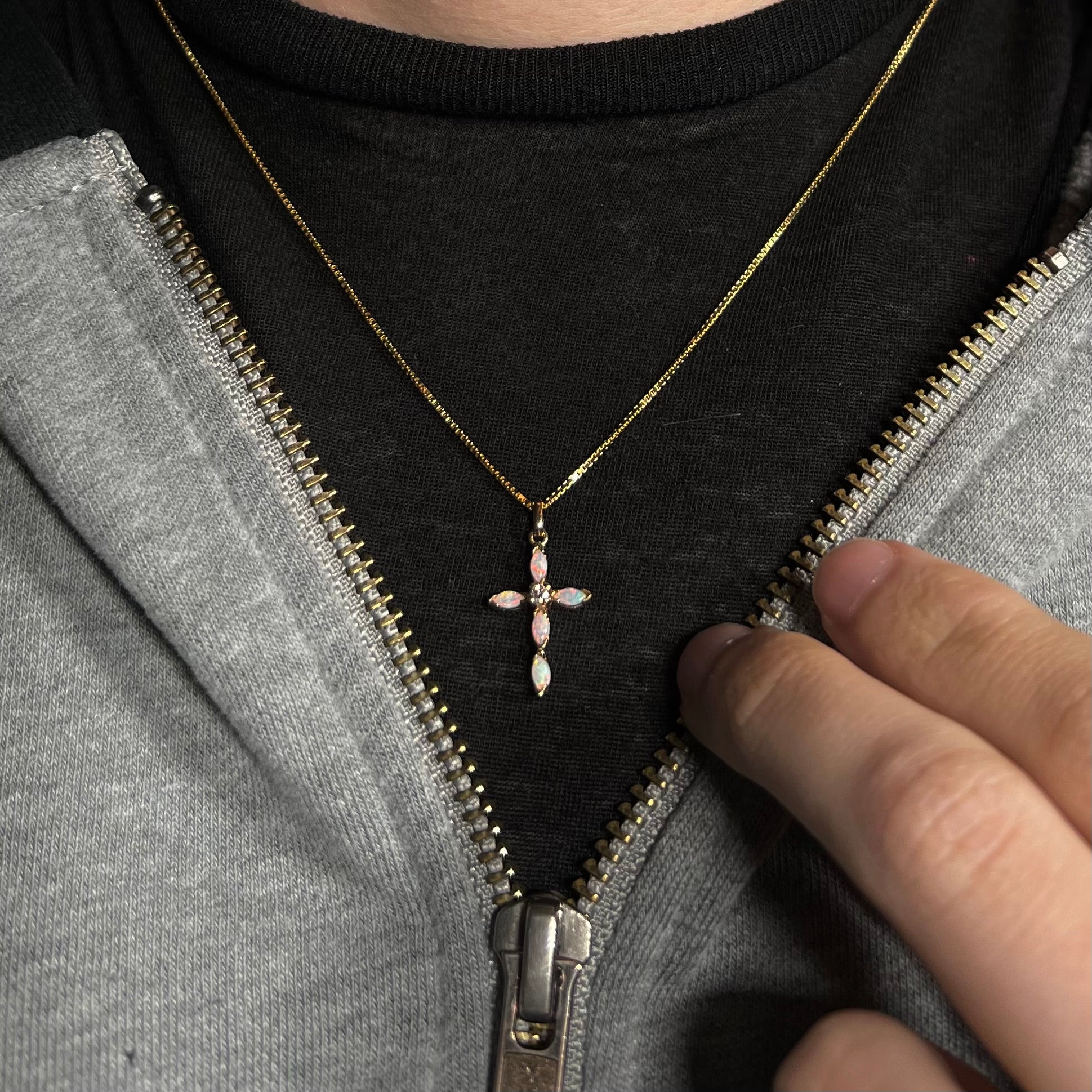A dainty opal and diamond cross necklace worn against a black shirt.