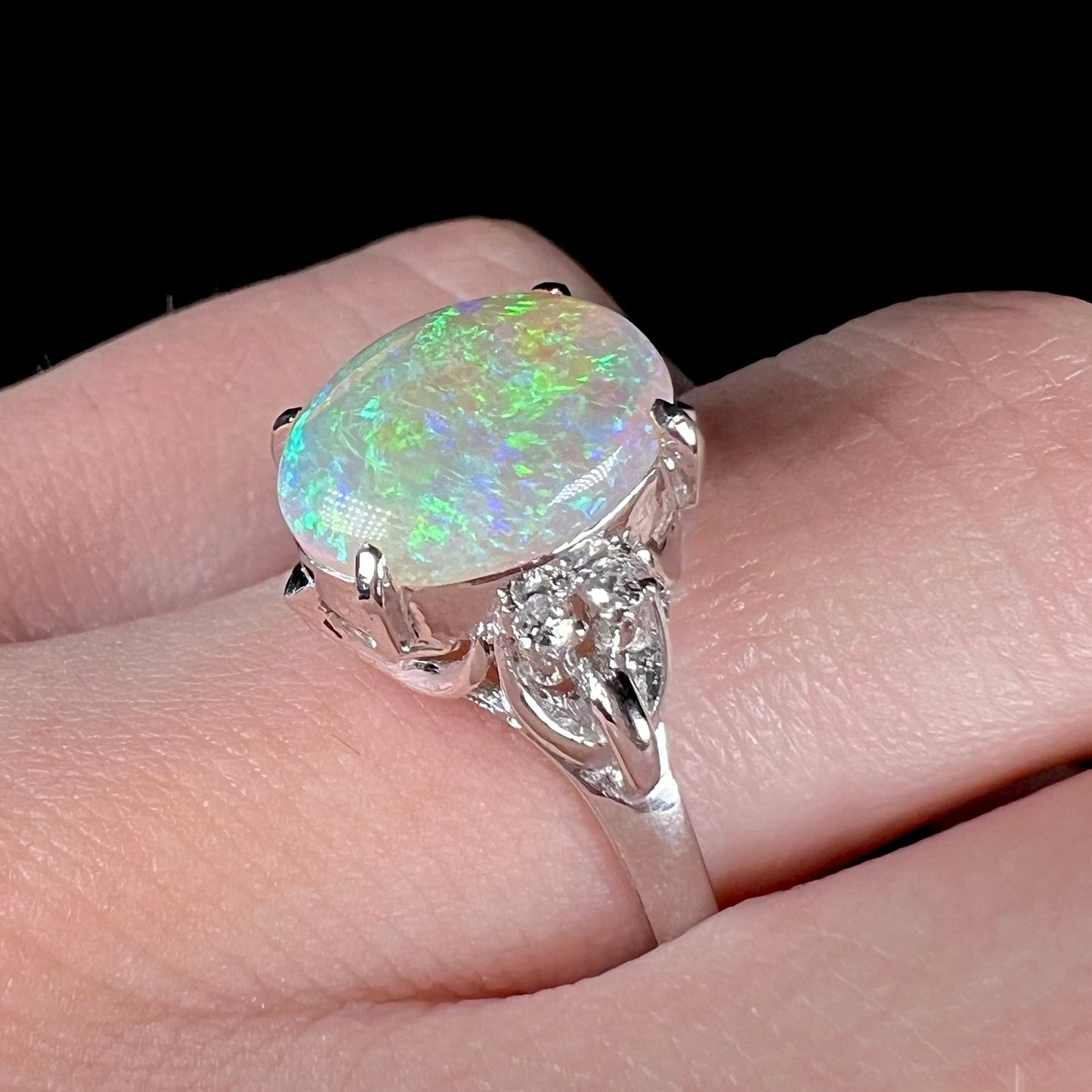 An Australian crystal opal and diamond engagement ring set in a platinum filigree mounting. The opal plays green/blue colors and has a crack.