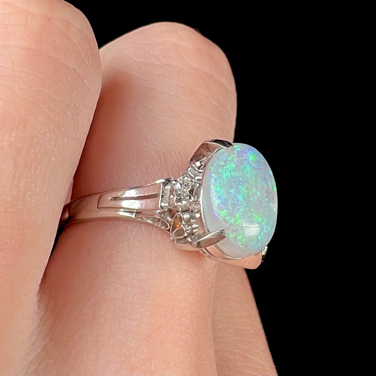 A platinum filigree opal engagement ring set with diamond accents. The opal has green-blue colors.
