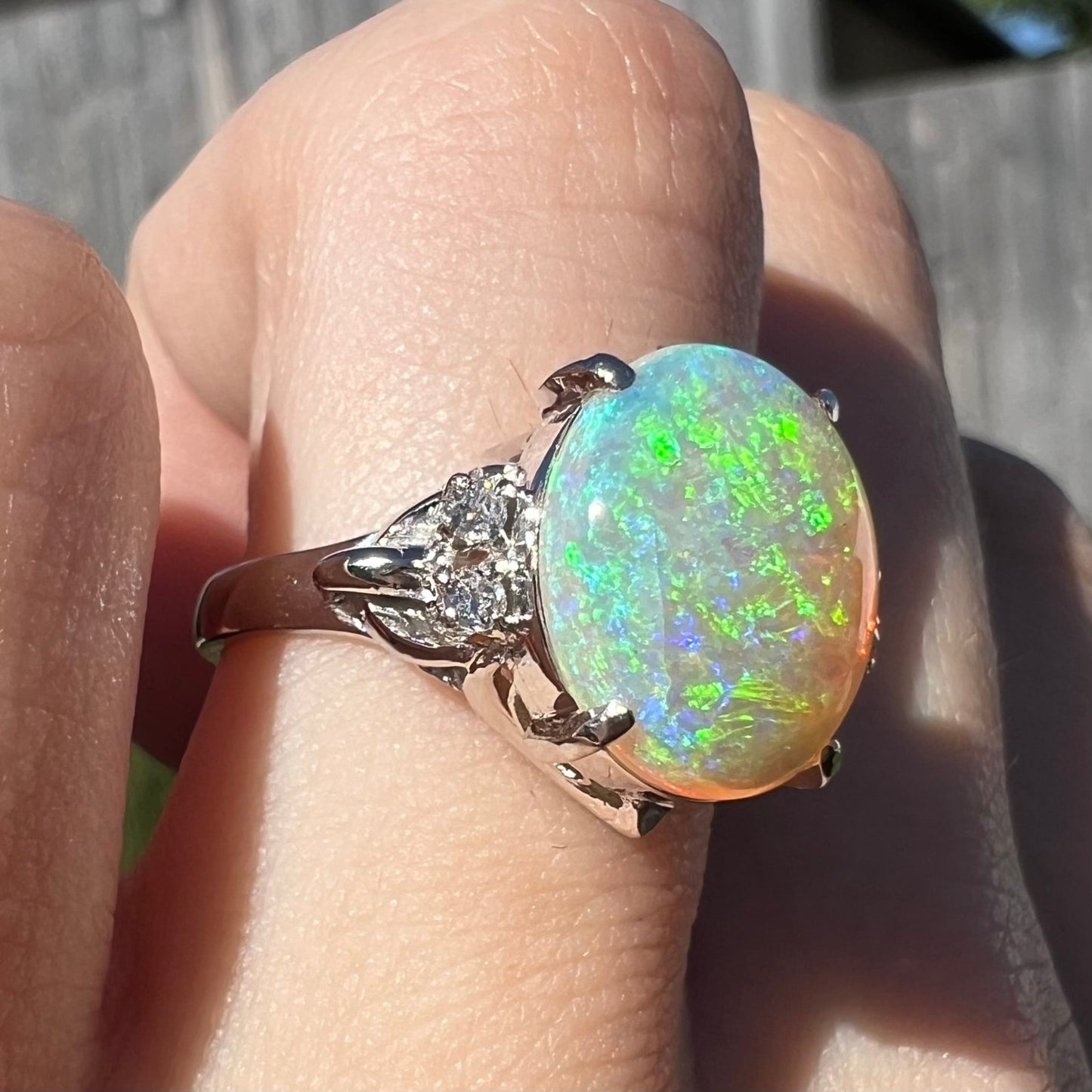 An Australian crystal opal engagement ring set with diamonds in a platinum filigree mounting. The opal plays green/blue colors and has a crack.